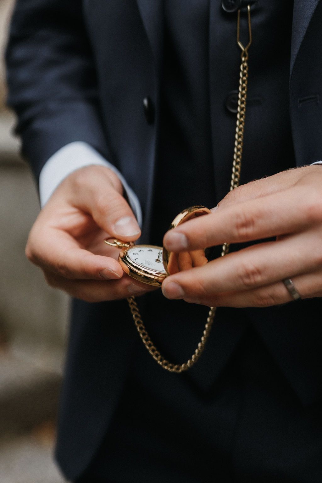 Close-up of groom holding an open gold pocket watch with chain at wedding ceremony.