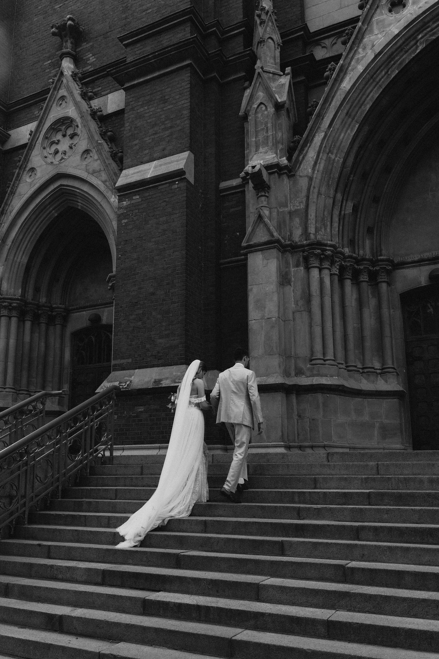 Bride and groom walking up stone steps of a Gothic church in a classic black and white wedding photo.