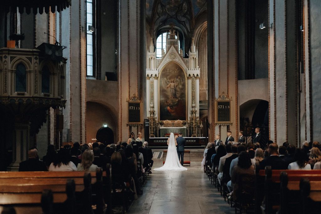 Elegant church wedding ceremony with bride in long veil standing at ornate altar.