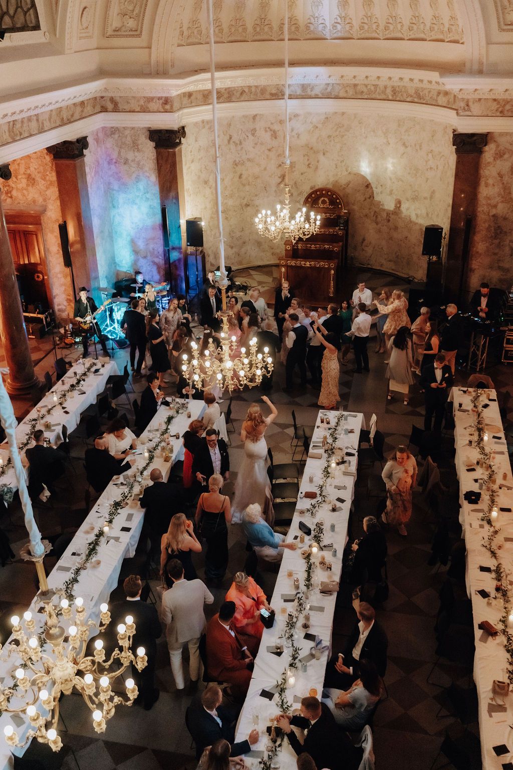 Aerial view of elegant wedding reception hall with long tables and chandelier lighting.