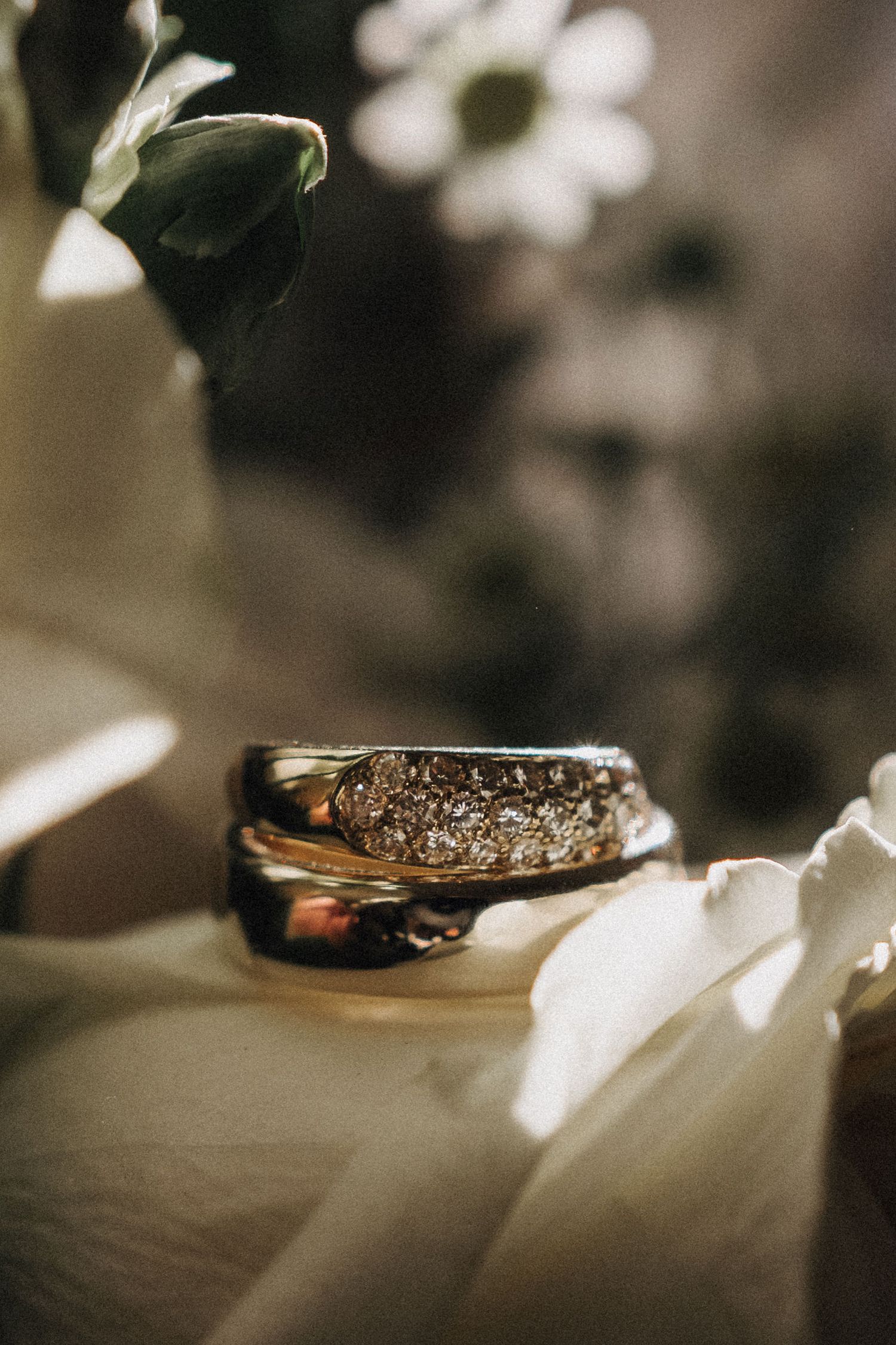 Close-up of stacked gold wedding rings with diamond detailing resting on white flower petals.