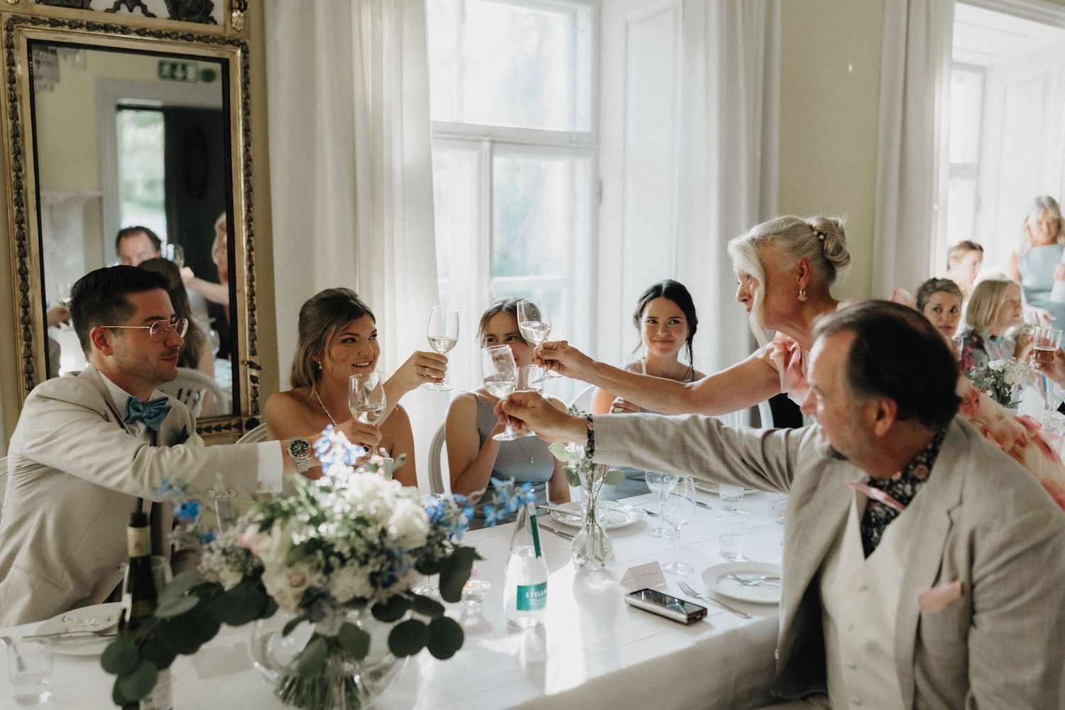 Wedding guests raising champagne glasses in a toast at an elegant reception dinner table with white floral centerpieces.
