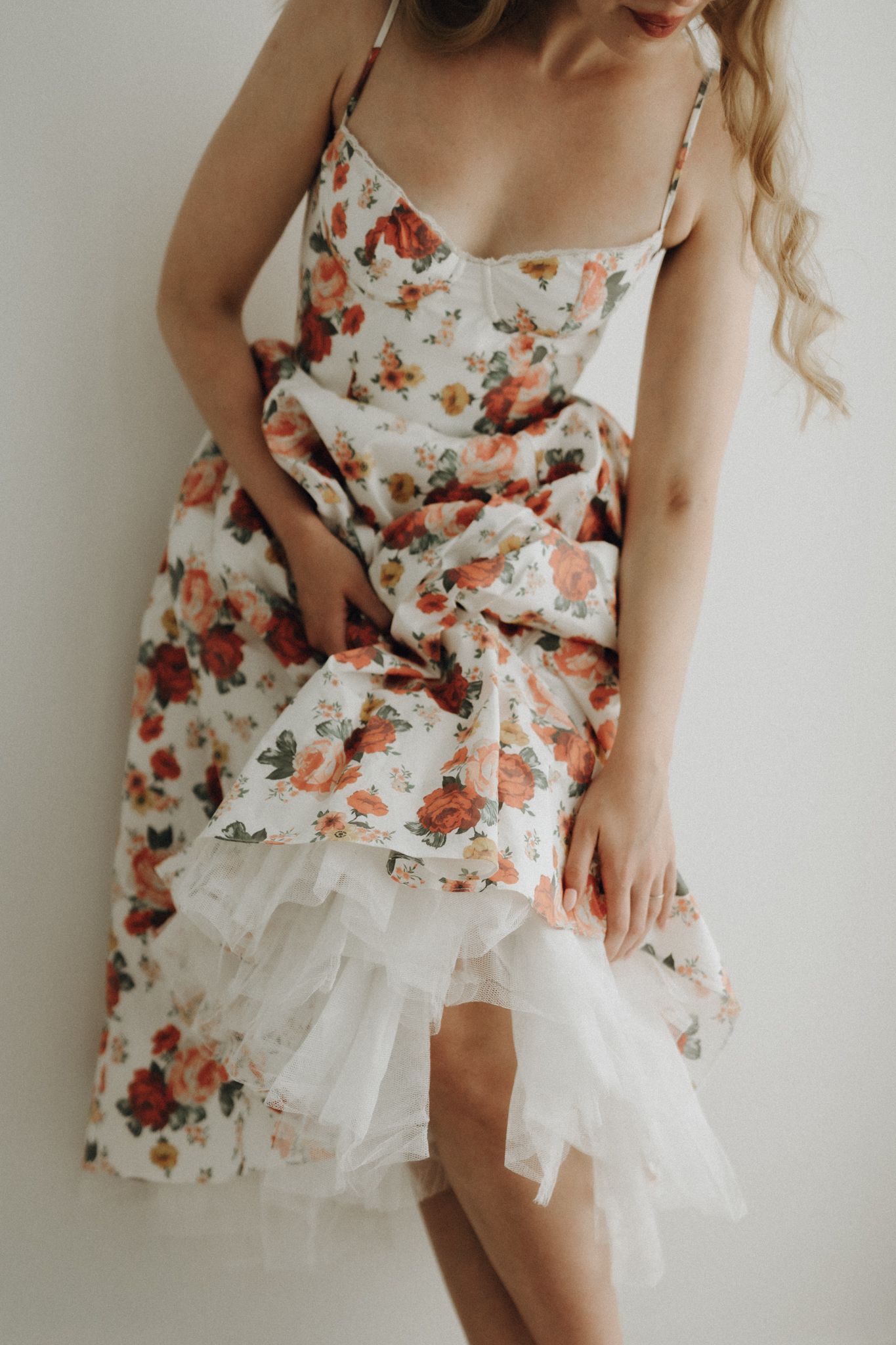 Woman in floral rose print corset dress with white tulle hem standing against white wall.