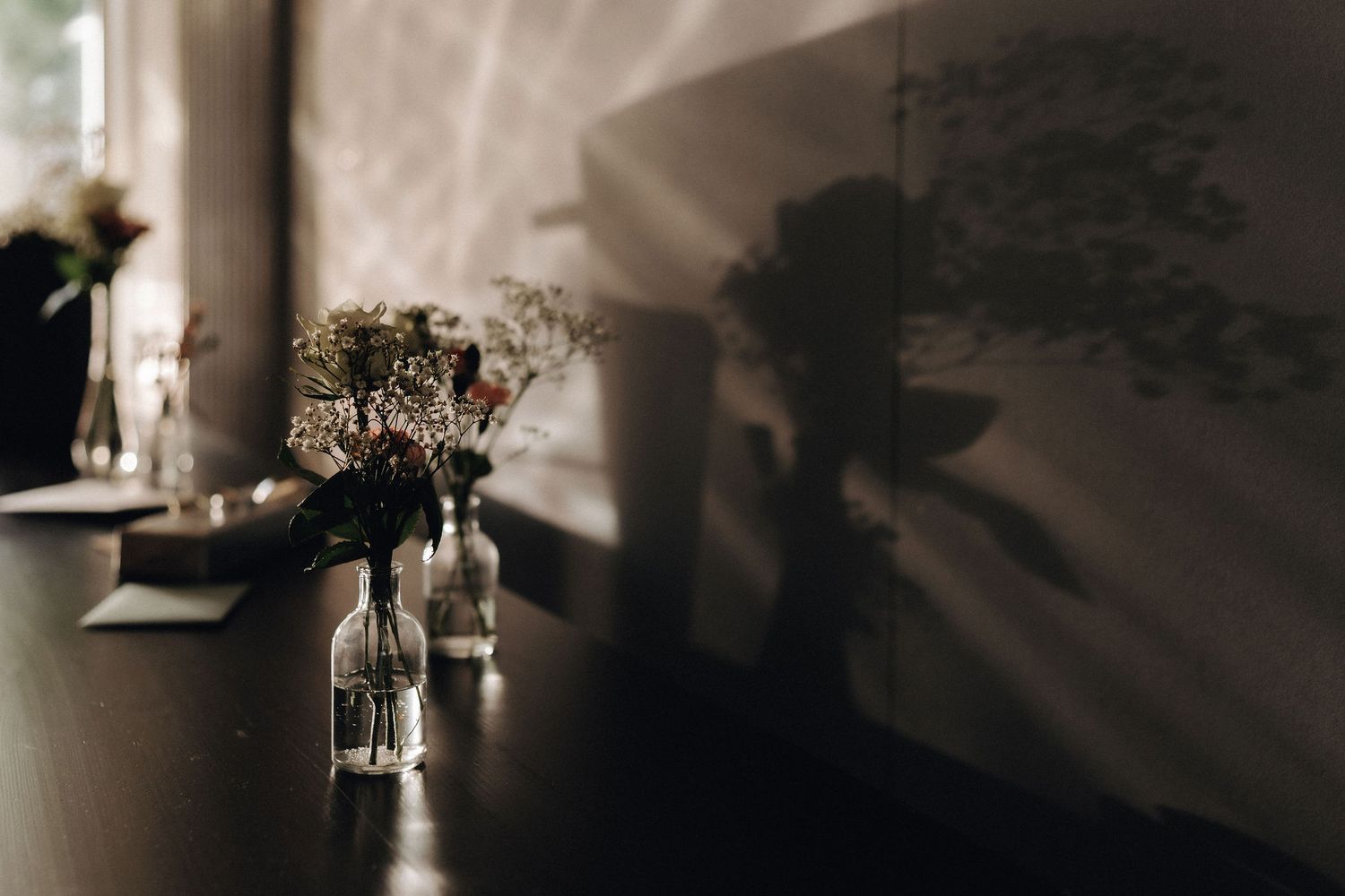 Small glass bud vases with delicate flowers casting shadows on a dark table surface.