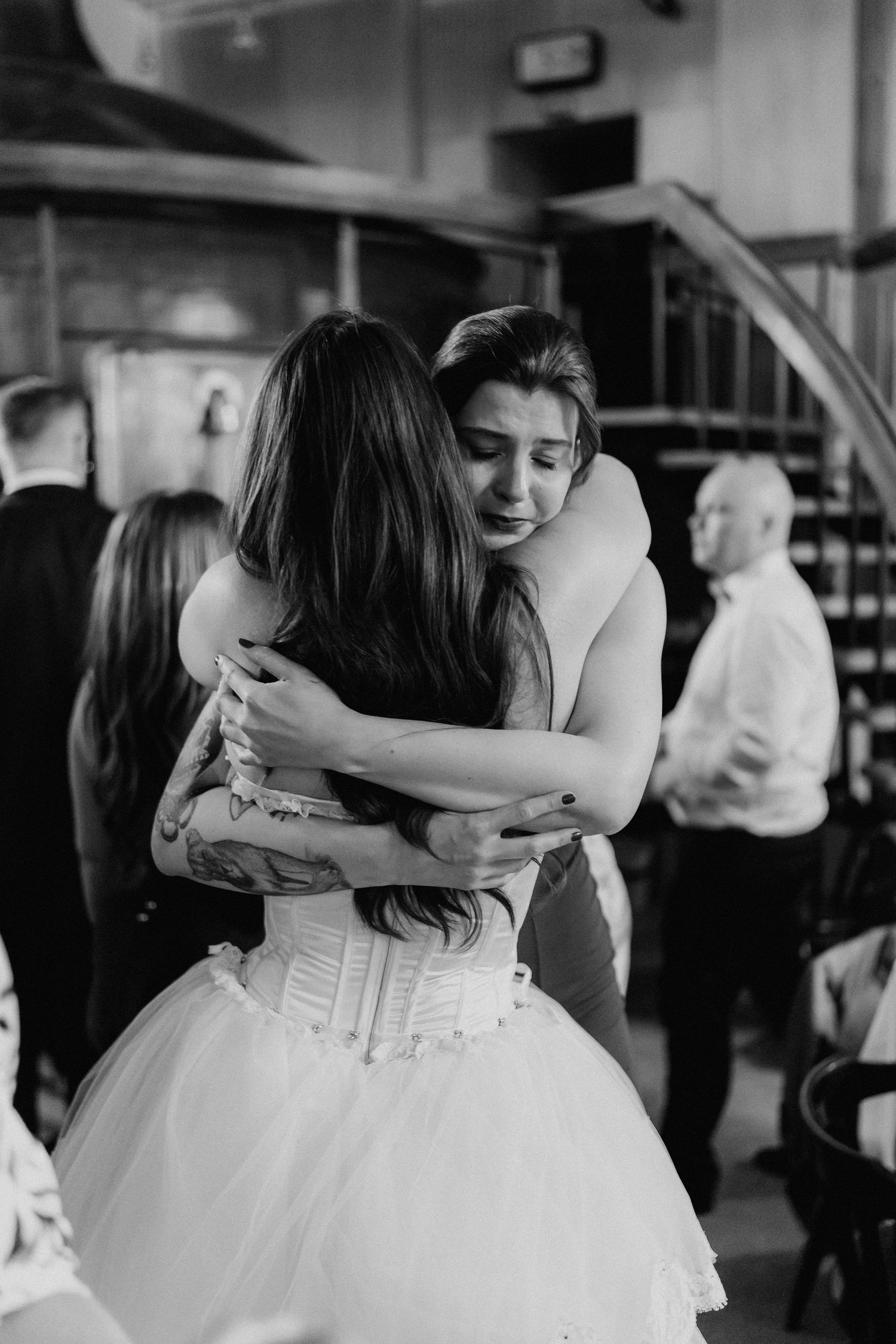 Bride and guest share a heartfelt hug at a wedding reception in black and white photo.