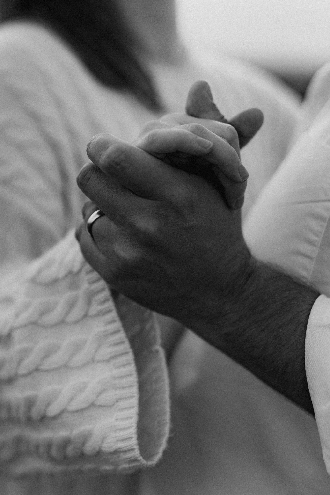 Black and white close-up of an engaged couple holding hands, showcasing a ring on the mans finger.