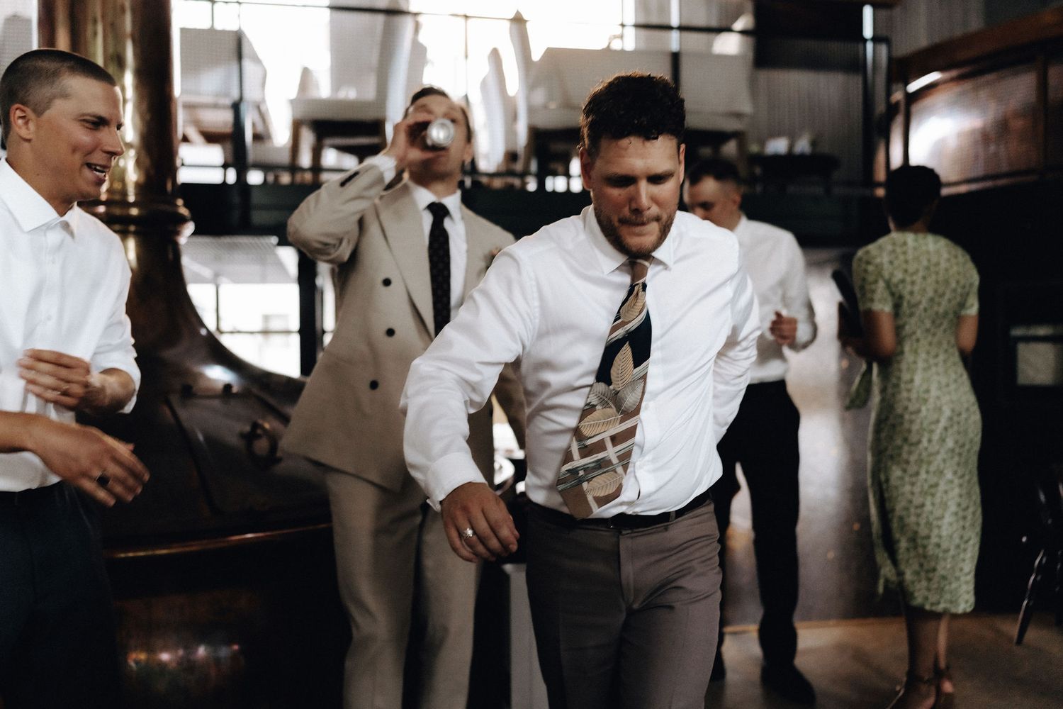 Groomsmen dancing and celebrating at a wedding reception in an industrial venue.