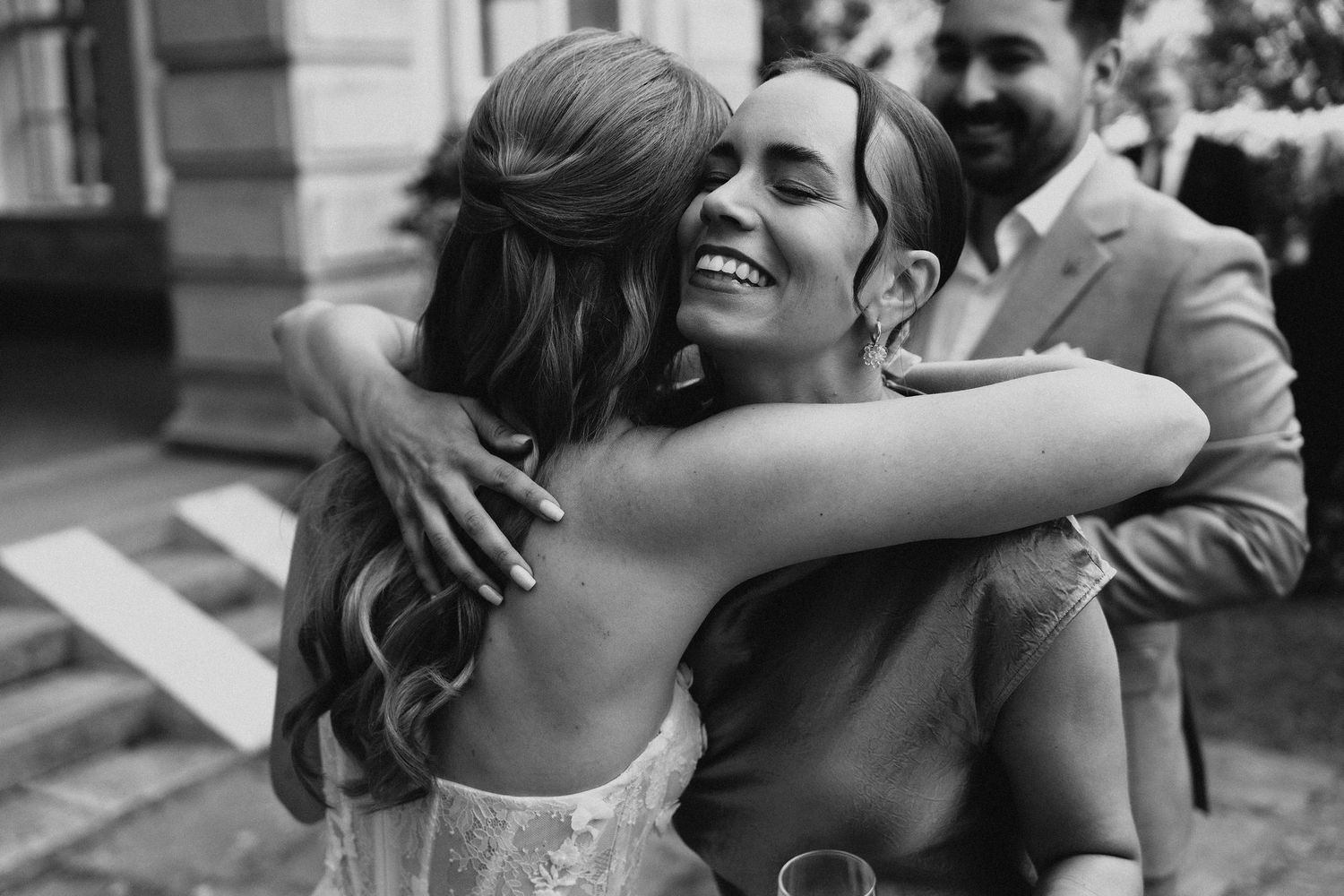 Black and white photo of a bride joyfully hugging a guest at her wedding reception outdoors.