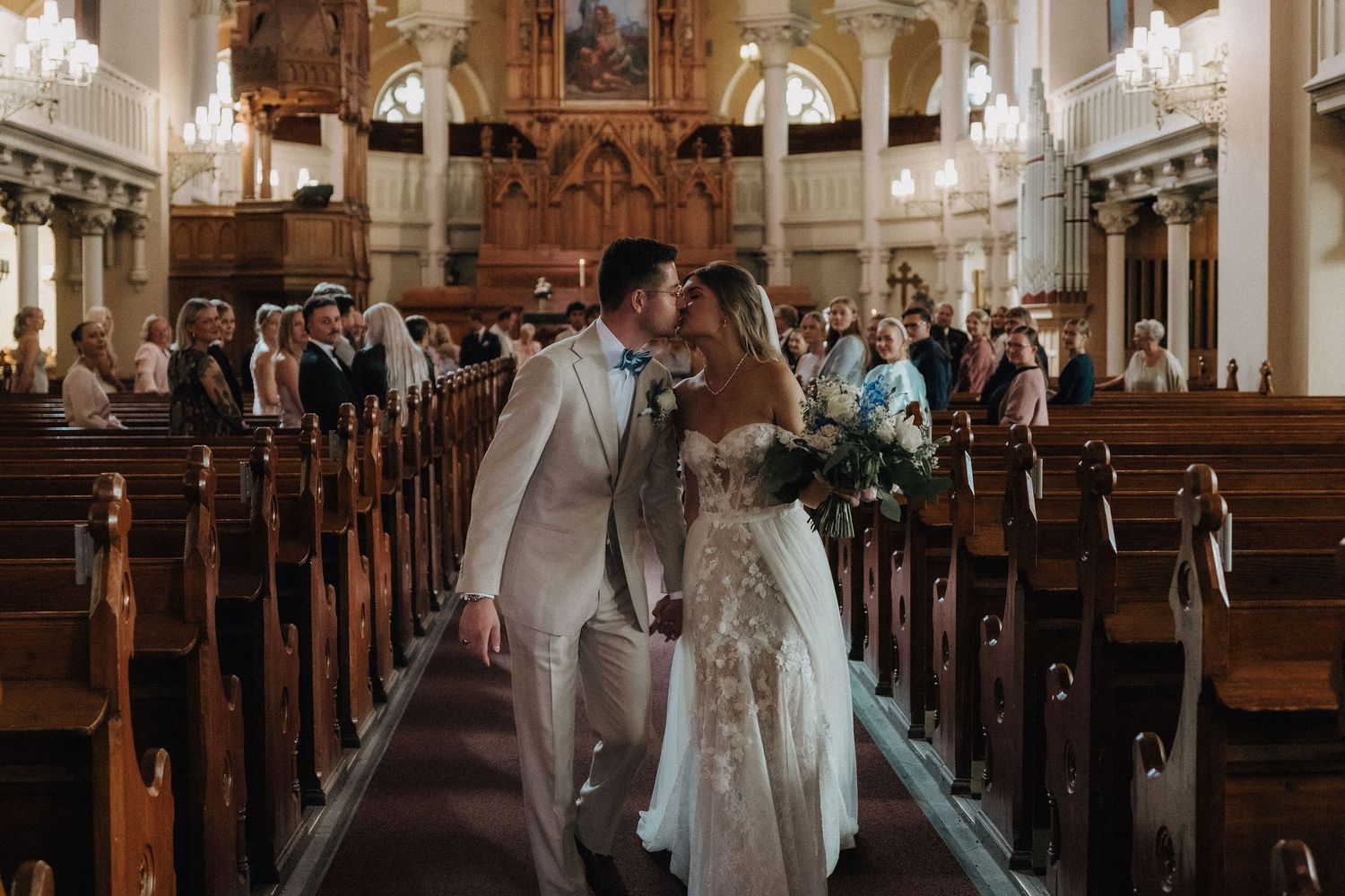 Bride and groom share a kiss while walking down the aisle of an ornate church.