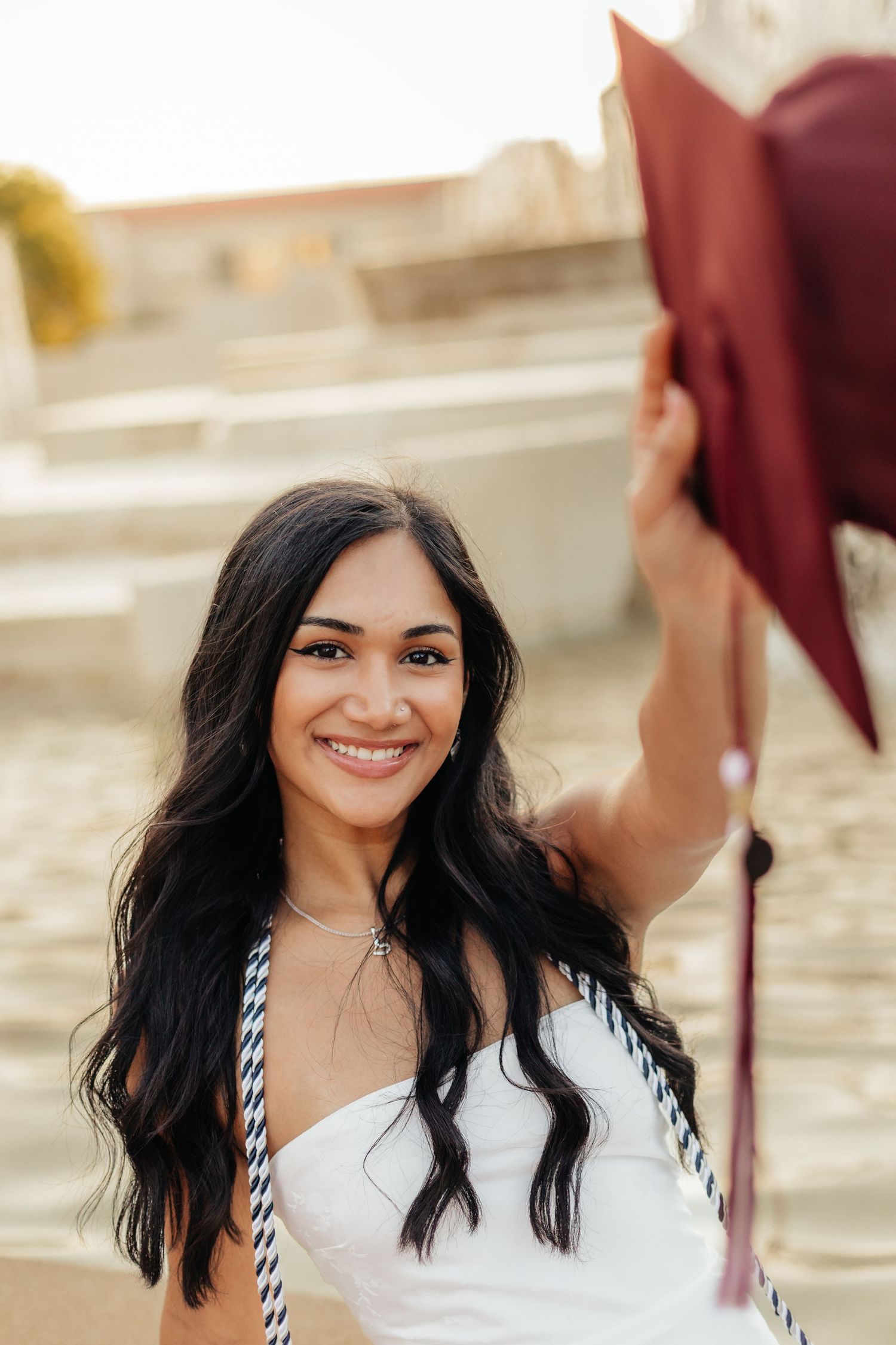 graduate holding cap wearing white dress and academic cords
