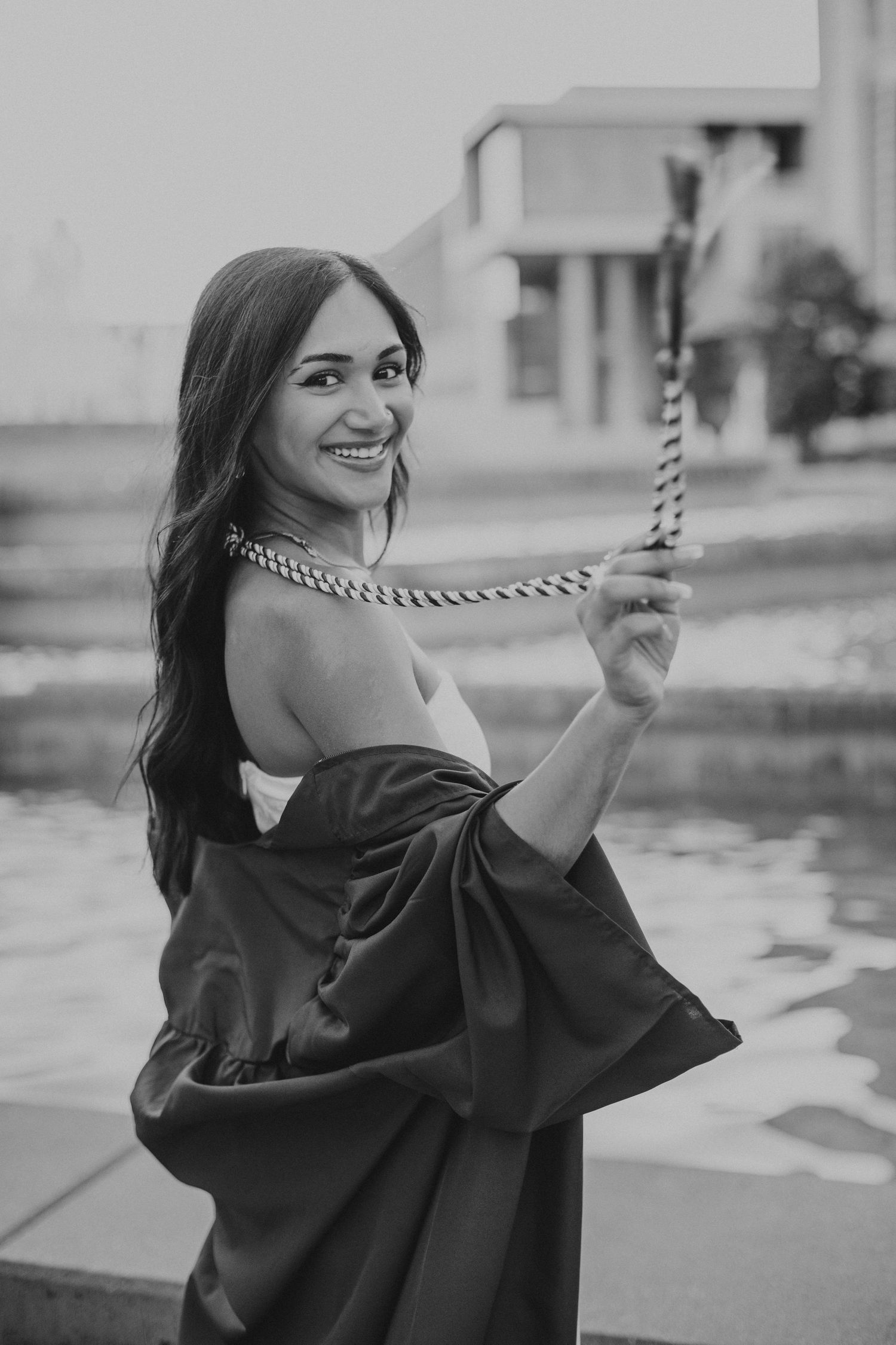black and white photo of woman wearing graduation gown holding her academic cords and swinging them