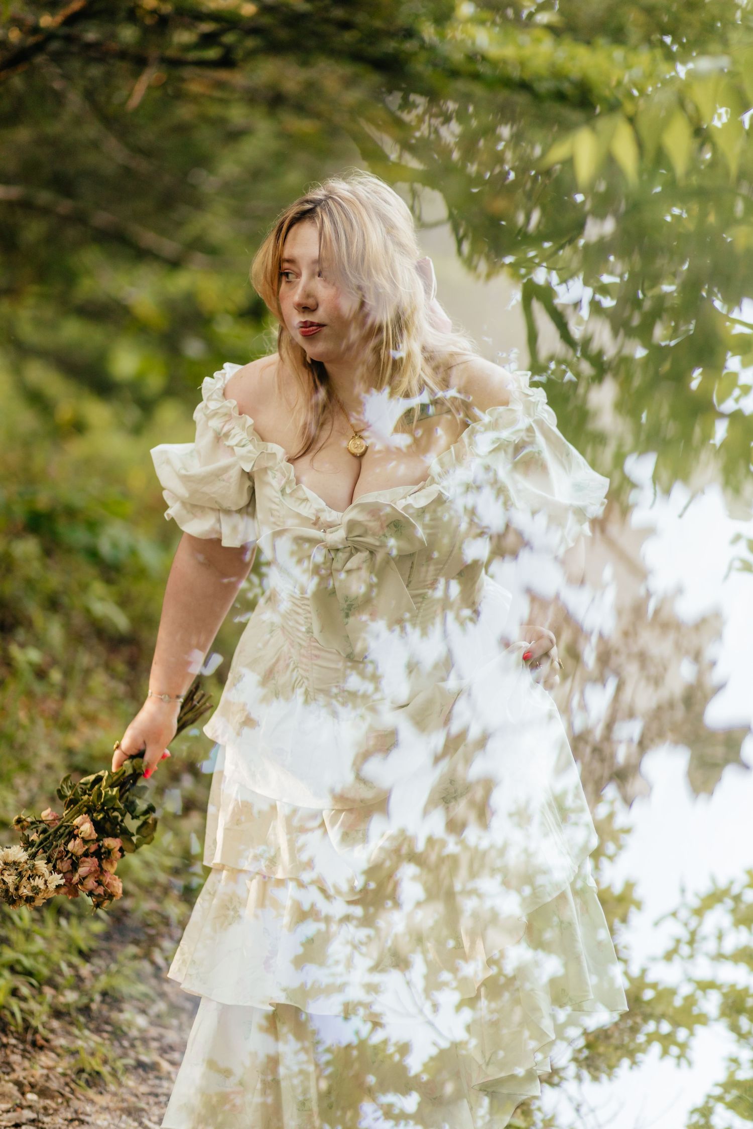 double exposure image of woman walking along trail with frilly dress holding dried flowers and a reflection of the sky