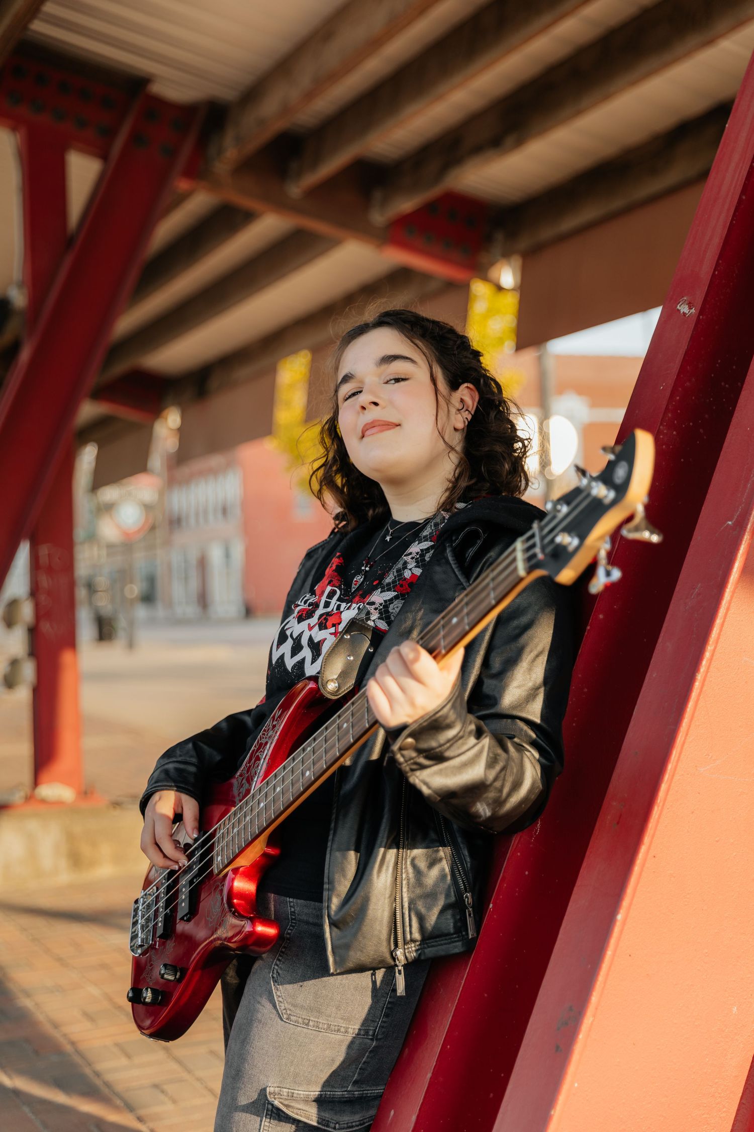 senior in leather jacket leaning against beam holding electric guitar