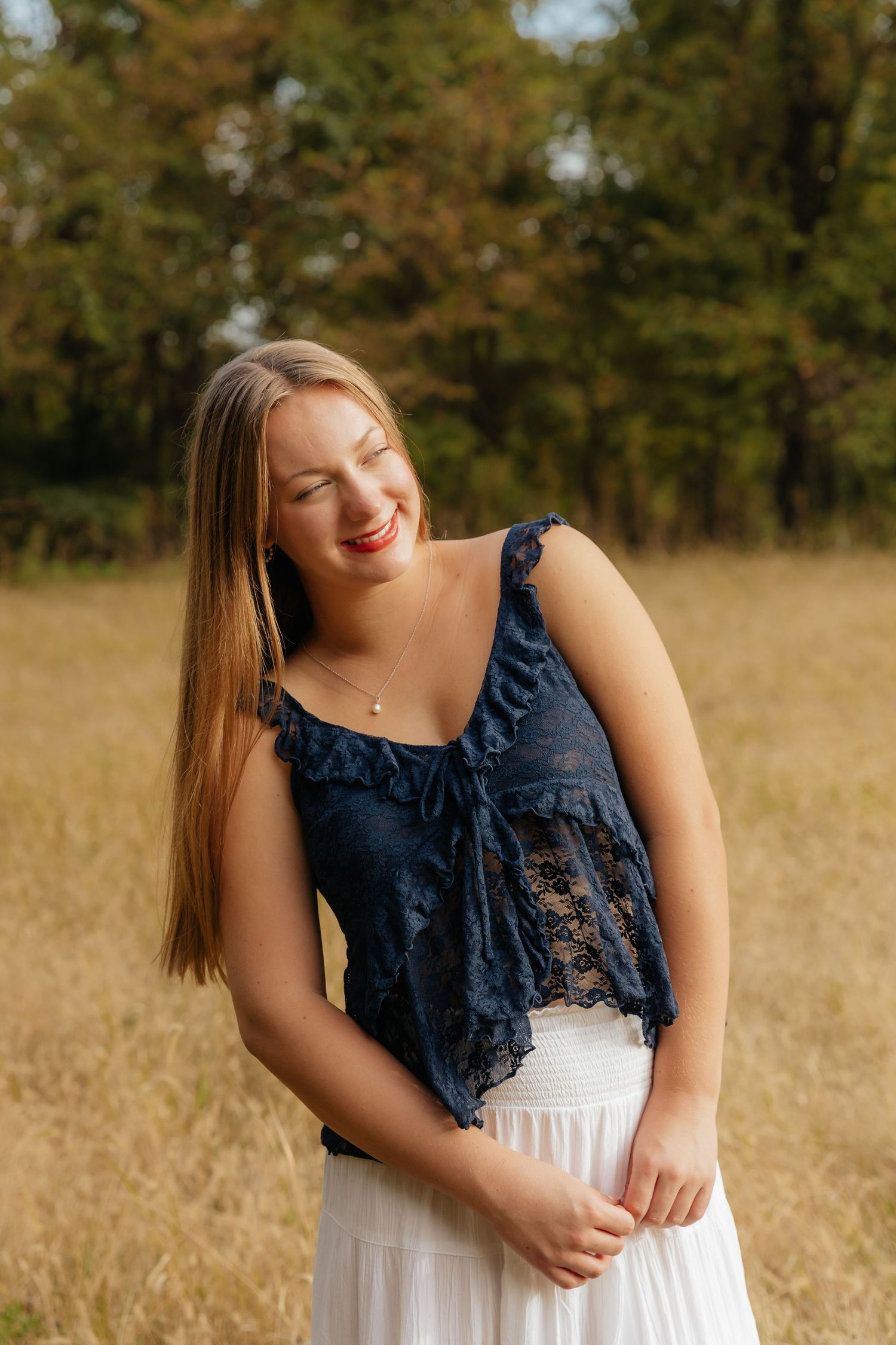 senior in blue lace top and white skirt in field