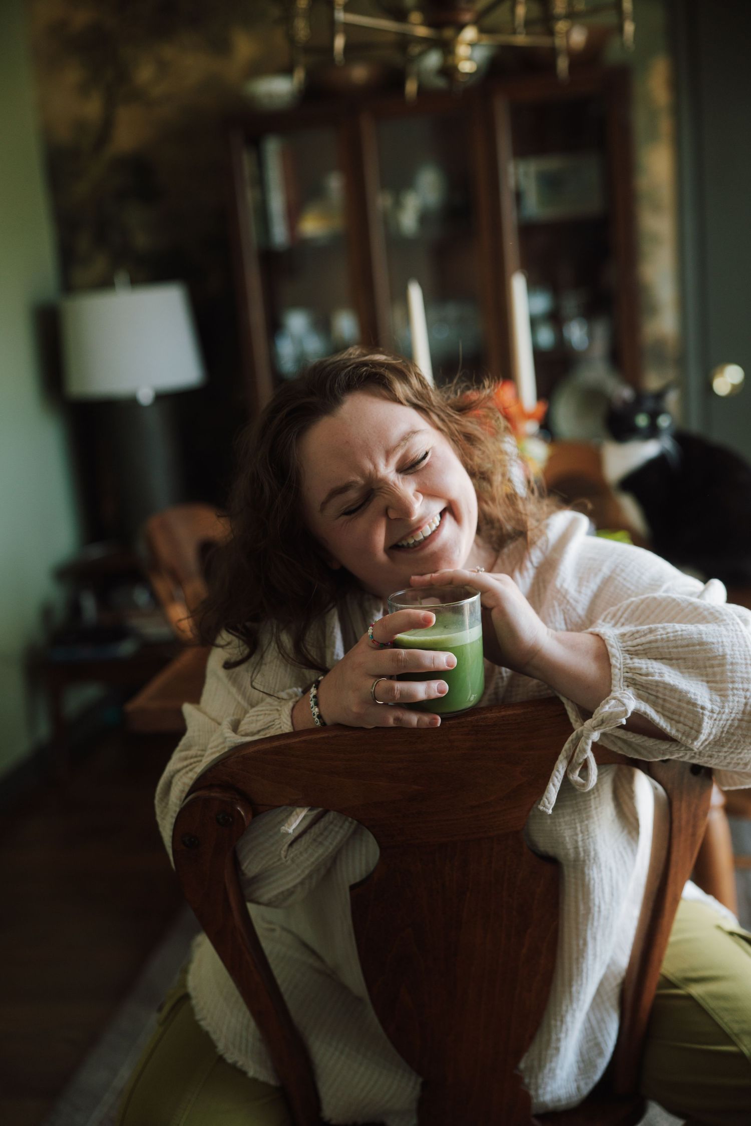 Leigh holding a glass of matcha sitting backwards in a chair in dining room