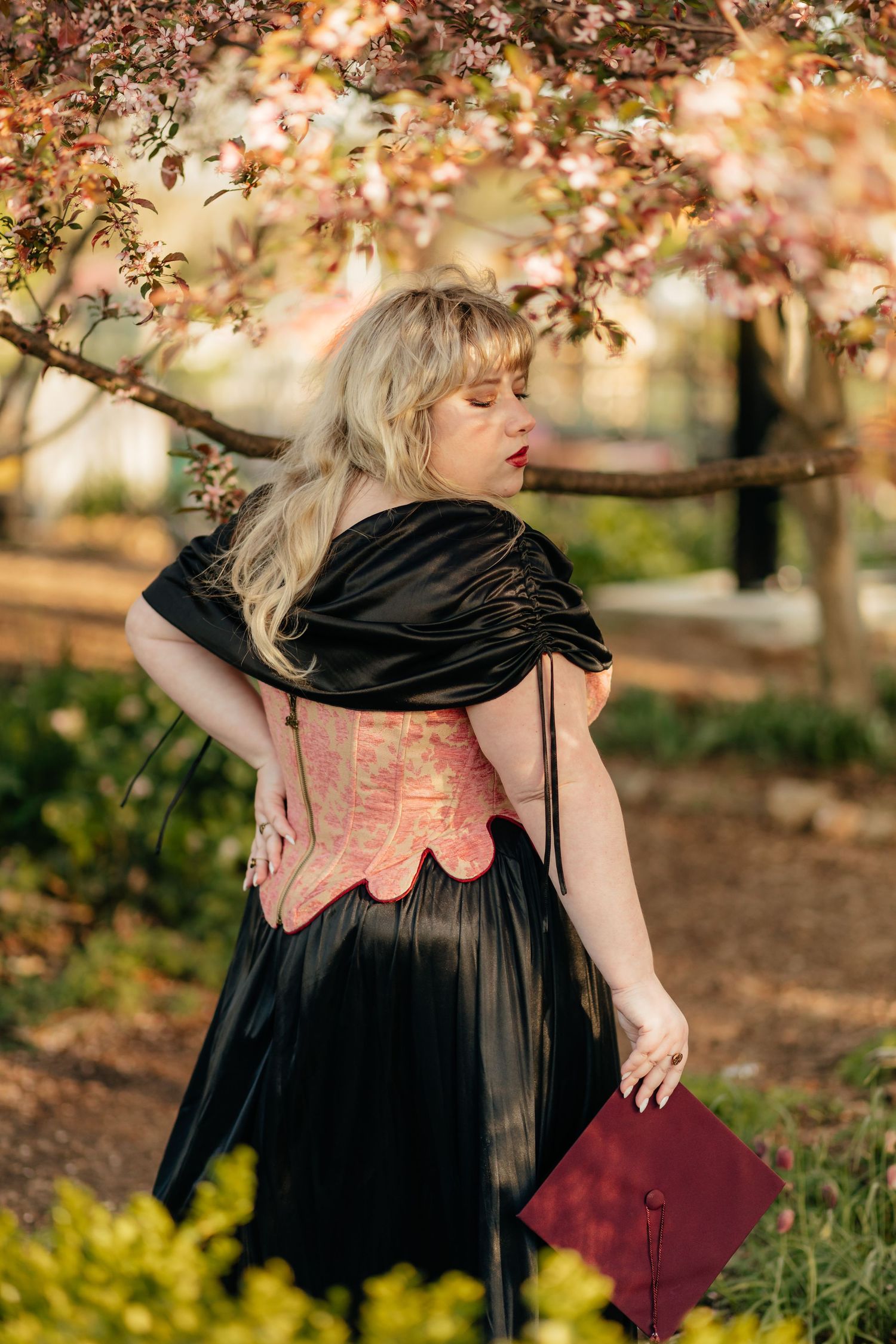 spring session grad in renaissance style fashion holding graduation cap looking down at shoulder
