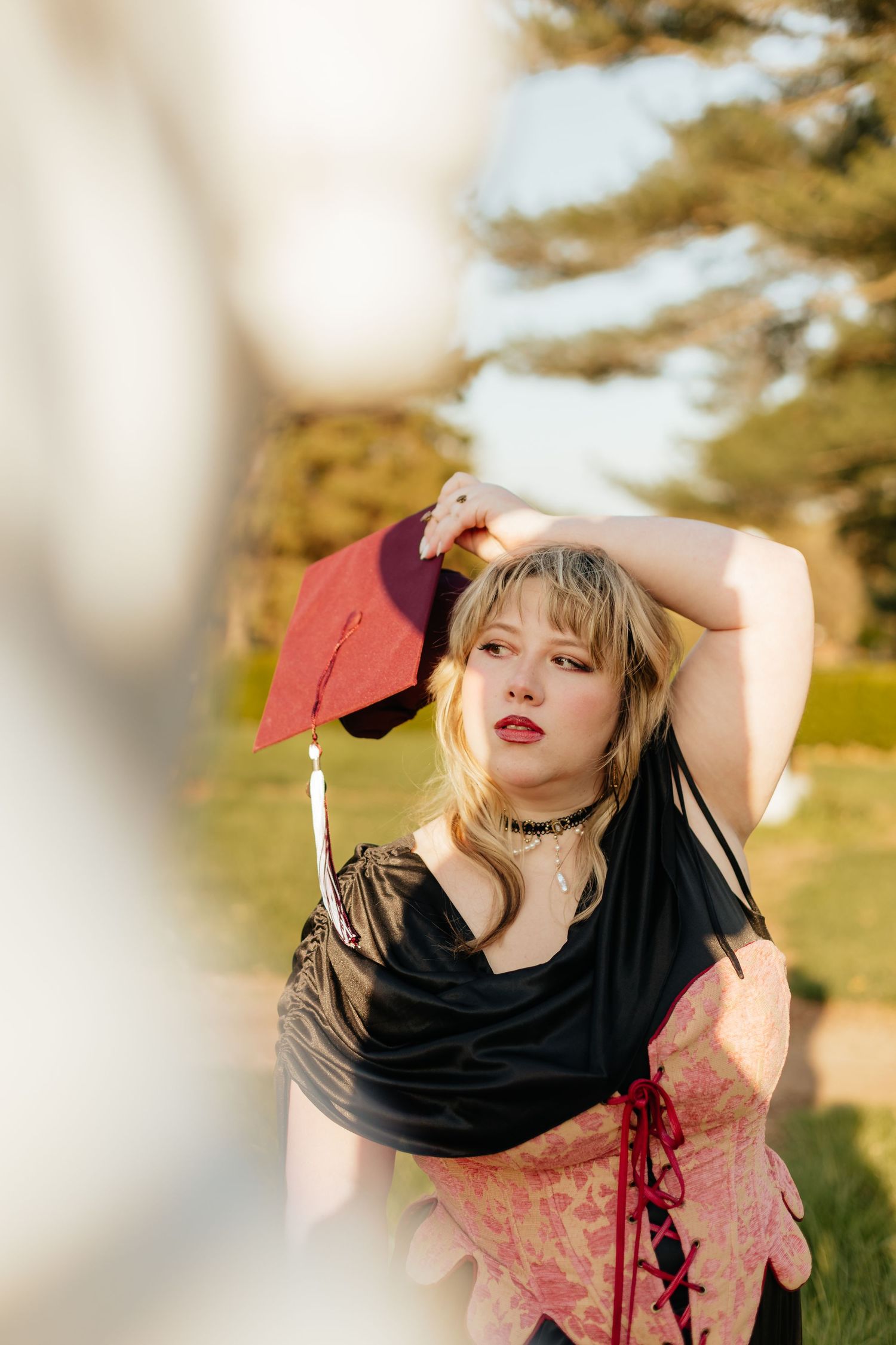 grad in renaissance style fashion holding graduation cap above her head looking away at sculpture