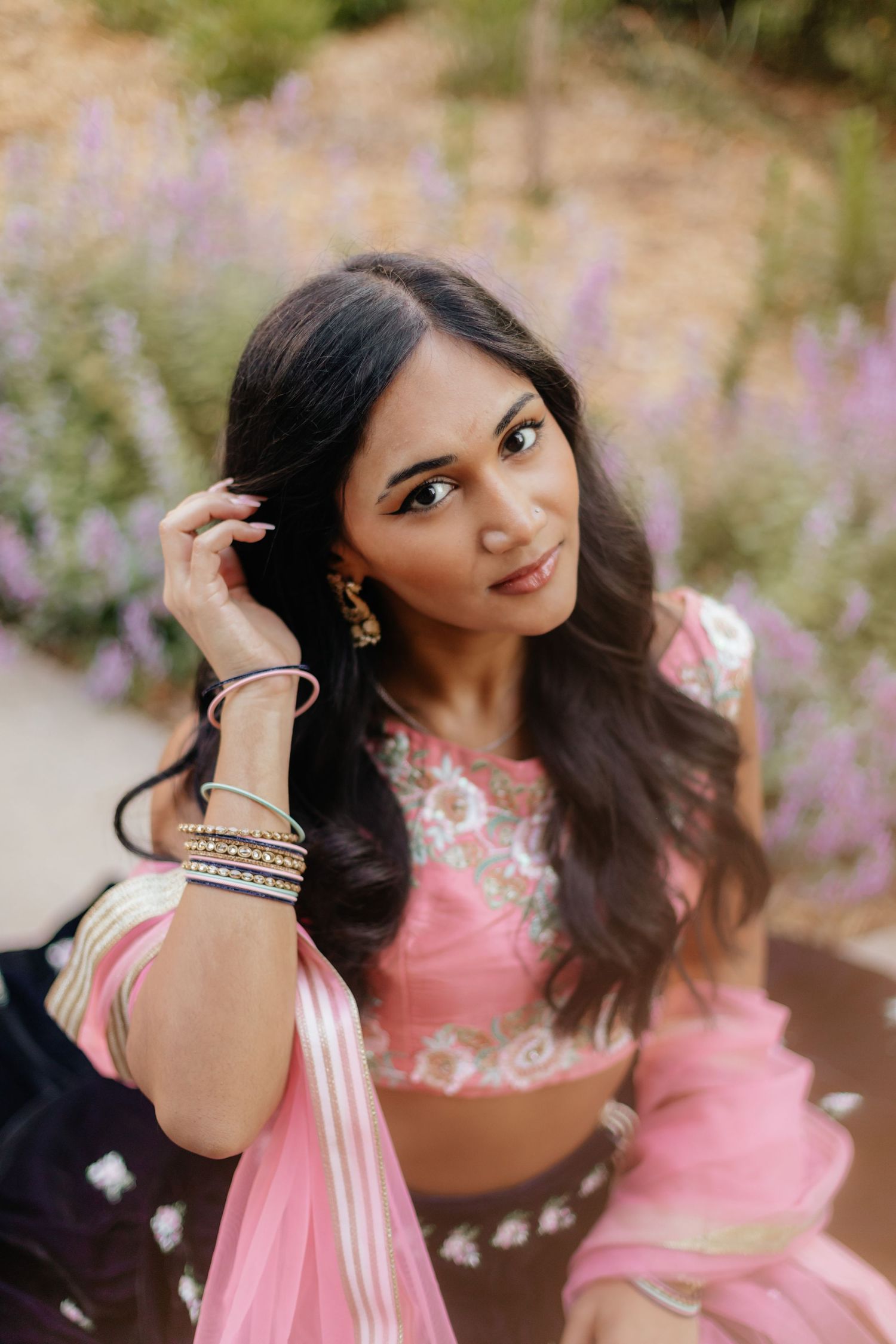 woman wearing traditional lehenga brushing hair out of her face and looking up at camera