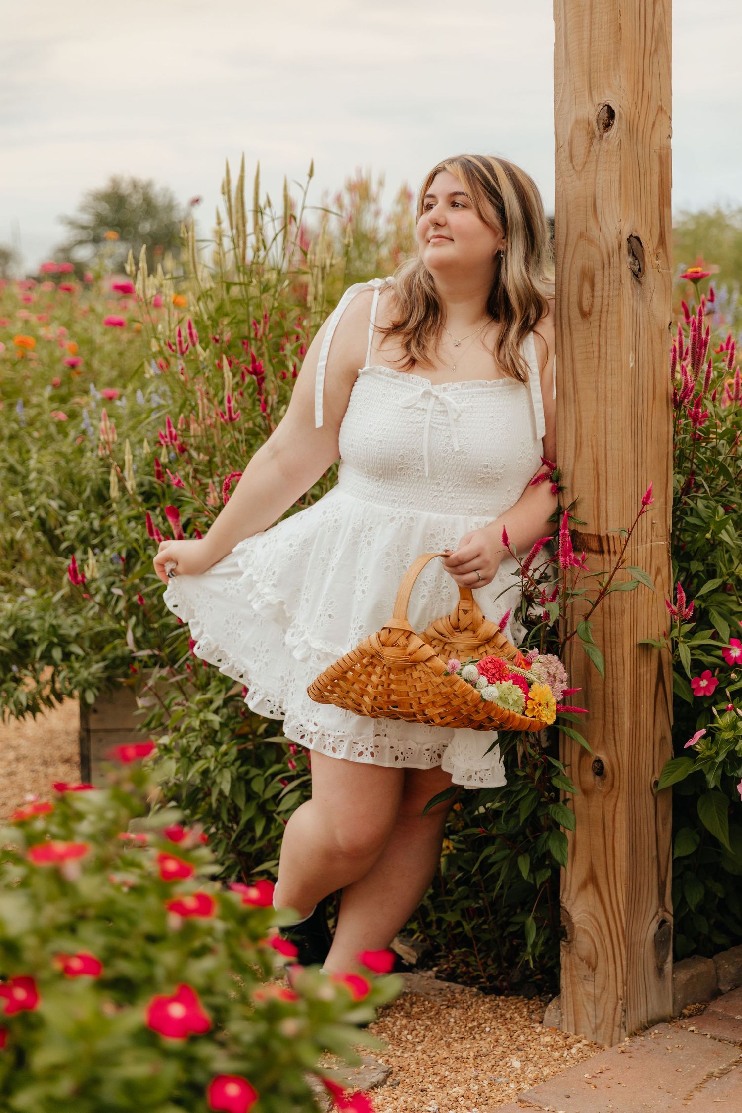 senior in flower garden holding a basket leaning against a wooden post