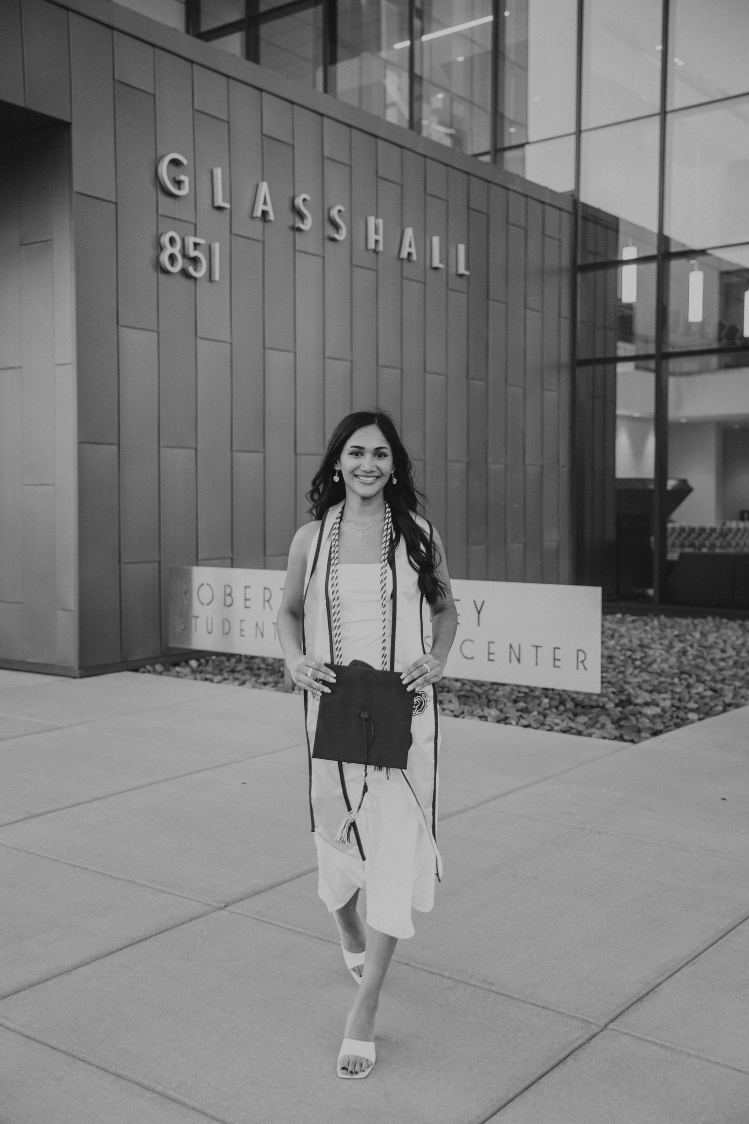 black and white image of grad standing in front of MSU Glass Hall holding cap