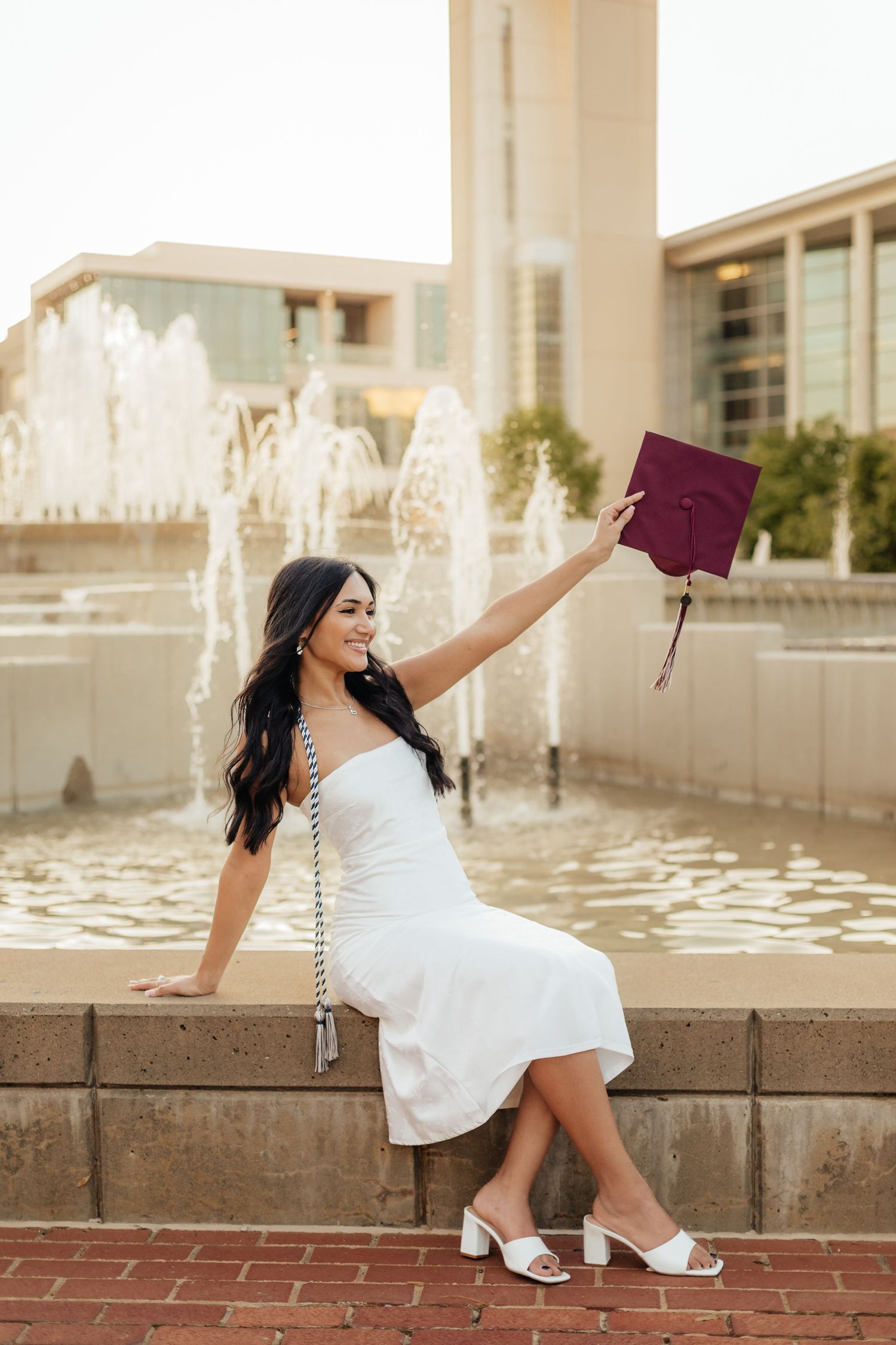 MSU grad sitting on ledge of fountain holding her grad cap