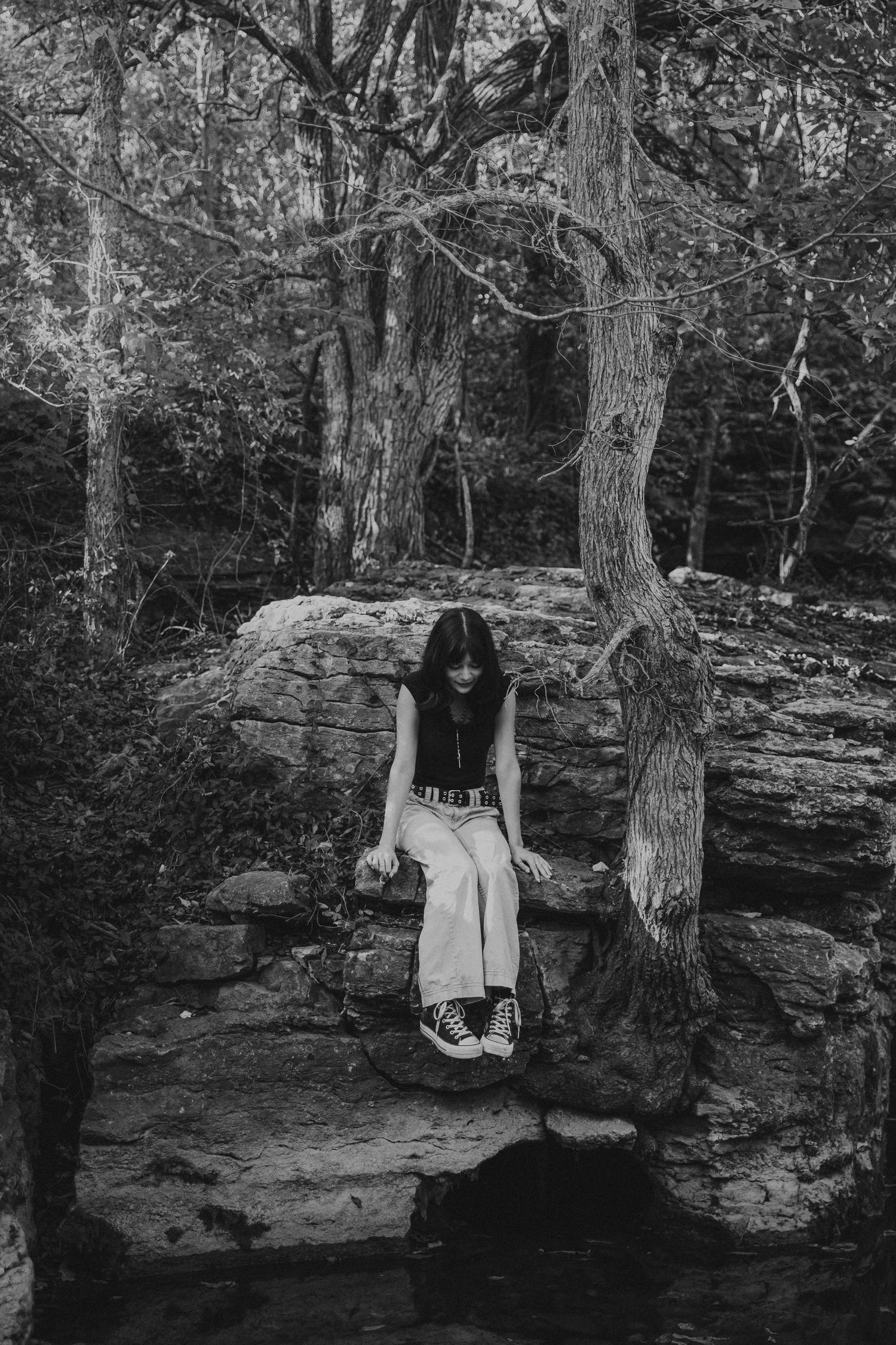 outdoor senior photo of girl looking down at water while sitting on rock formation