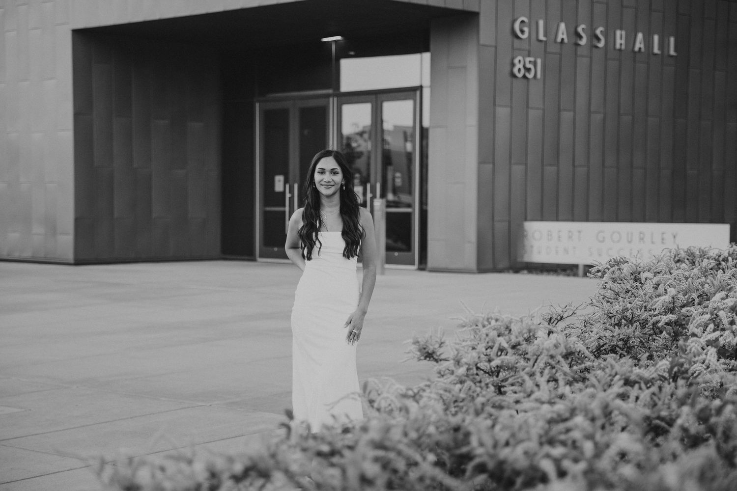 black and white photo of woman in white dress standing in front of Glass Hall MSU