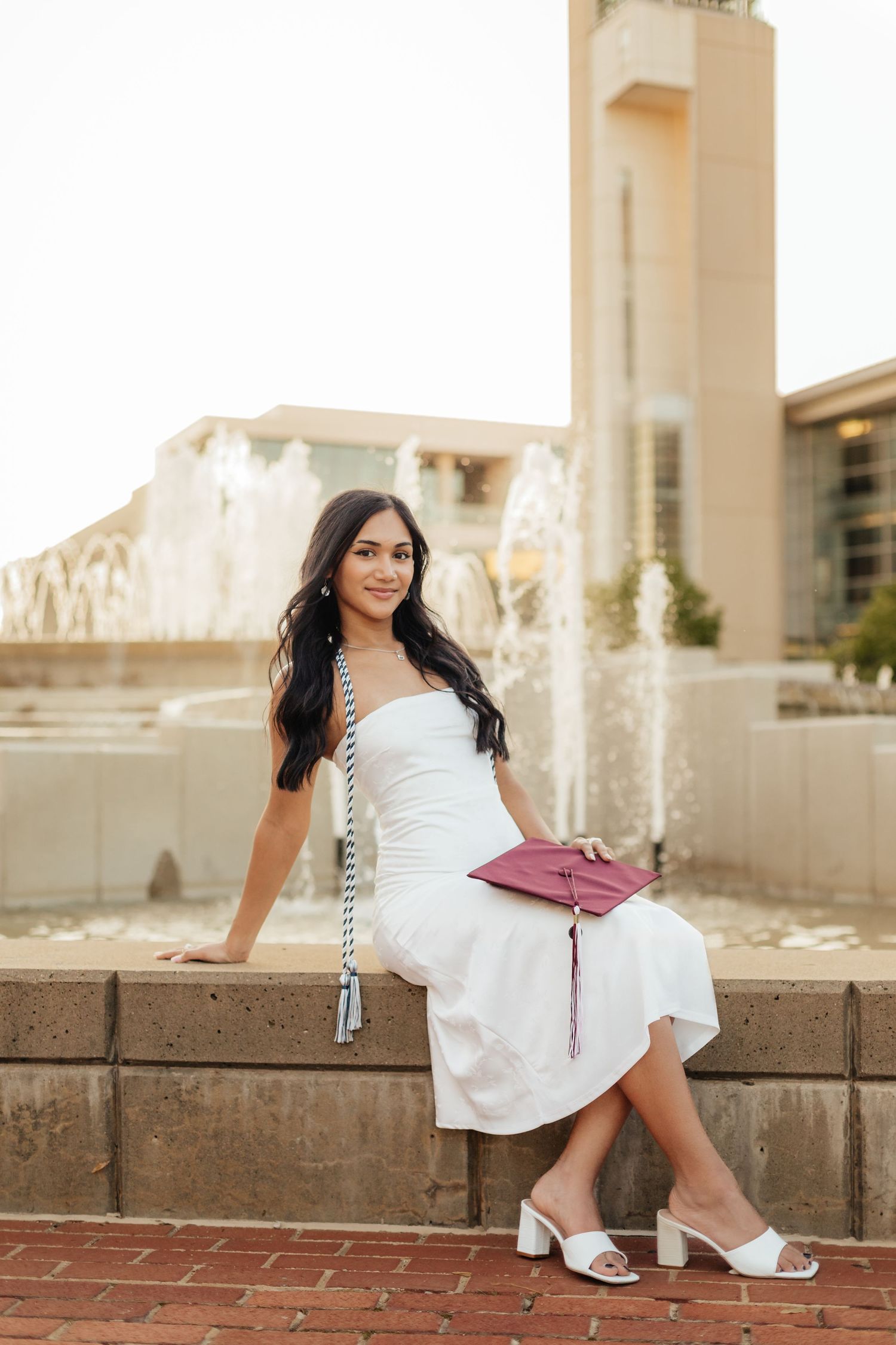 graduate sitting on MSU fountain with cap in her lap