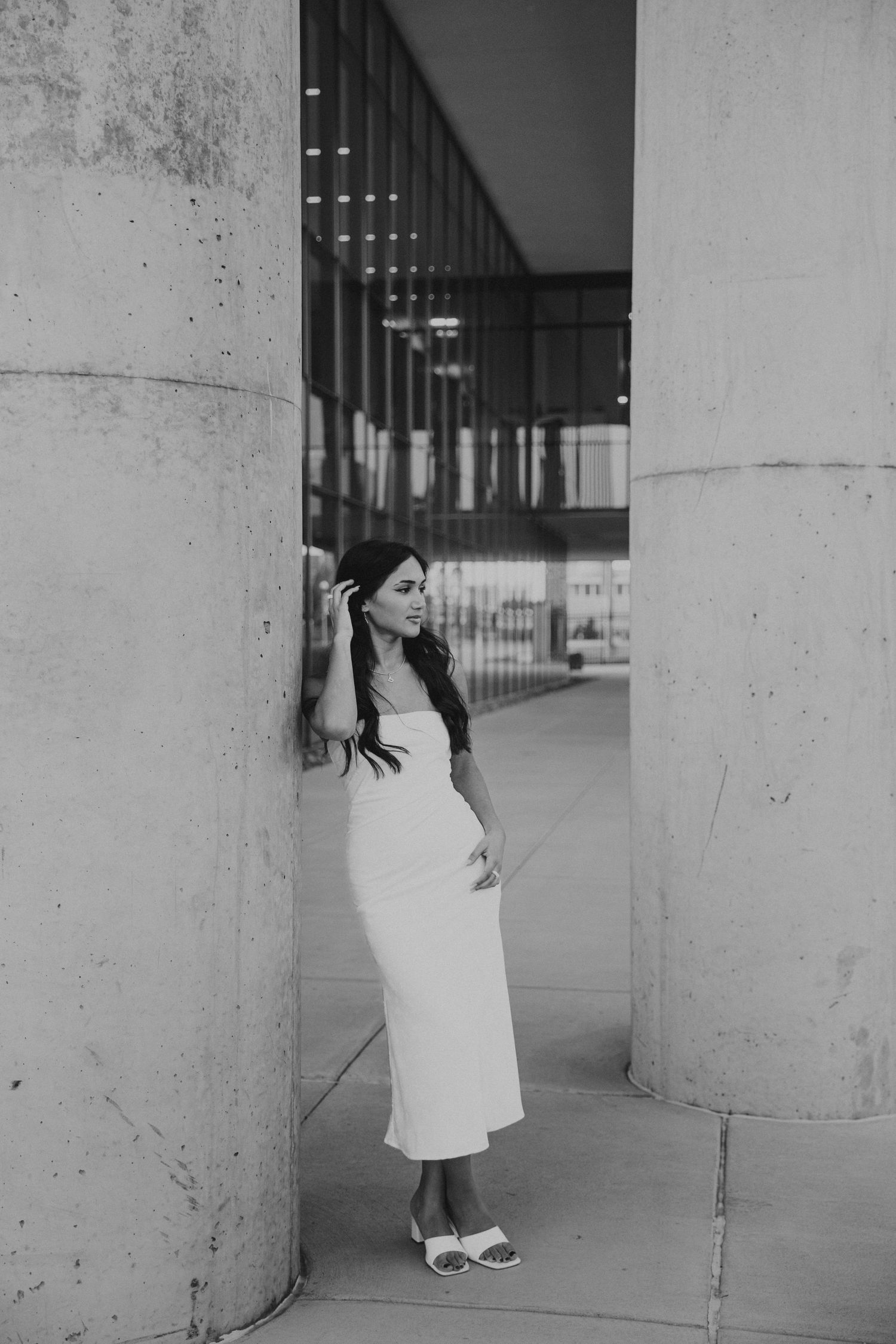MSU grad leaning against Glass Hall pillars wearing white dress