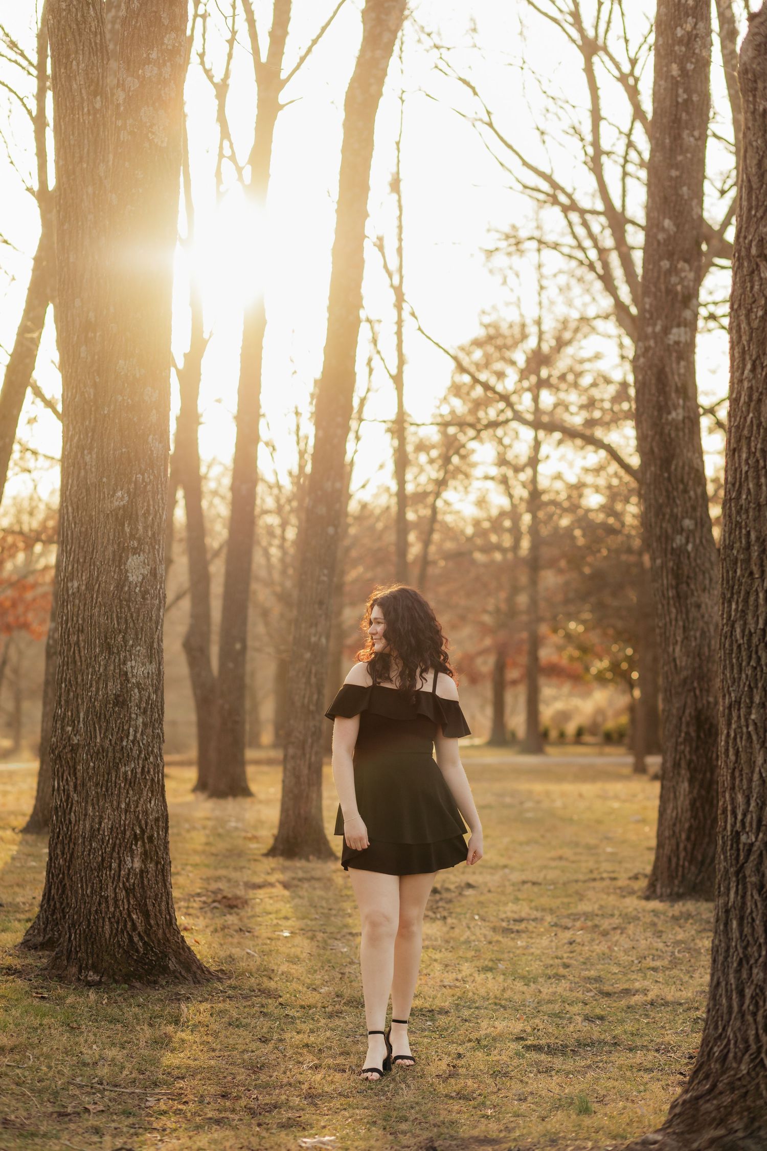 girl in black dress walking between tall skinny trees at Nathanael Greene in fall during golden hour