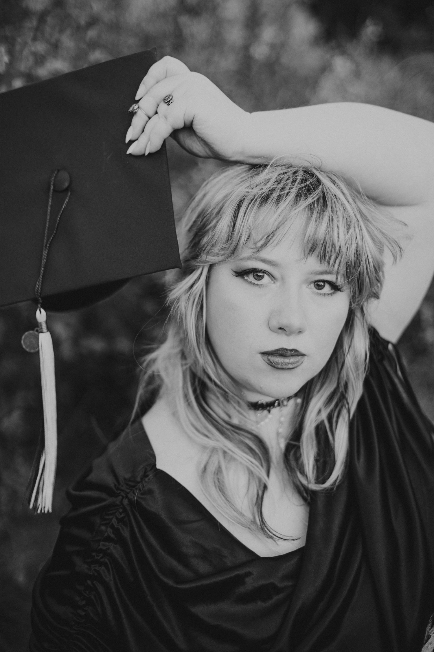 black and white photo of grad with shaggy haircut holding grad cap above her head