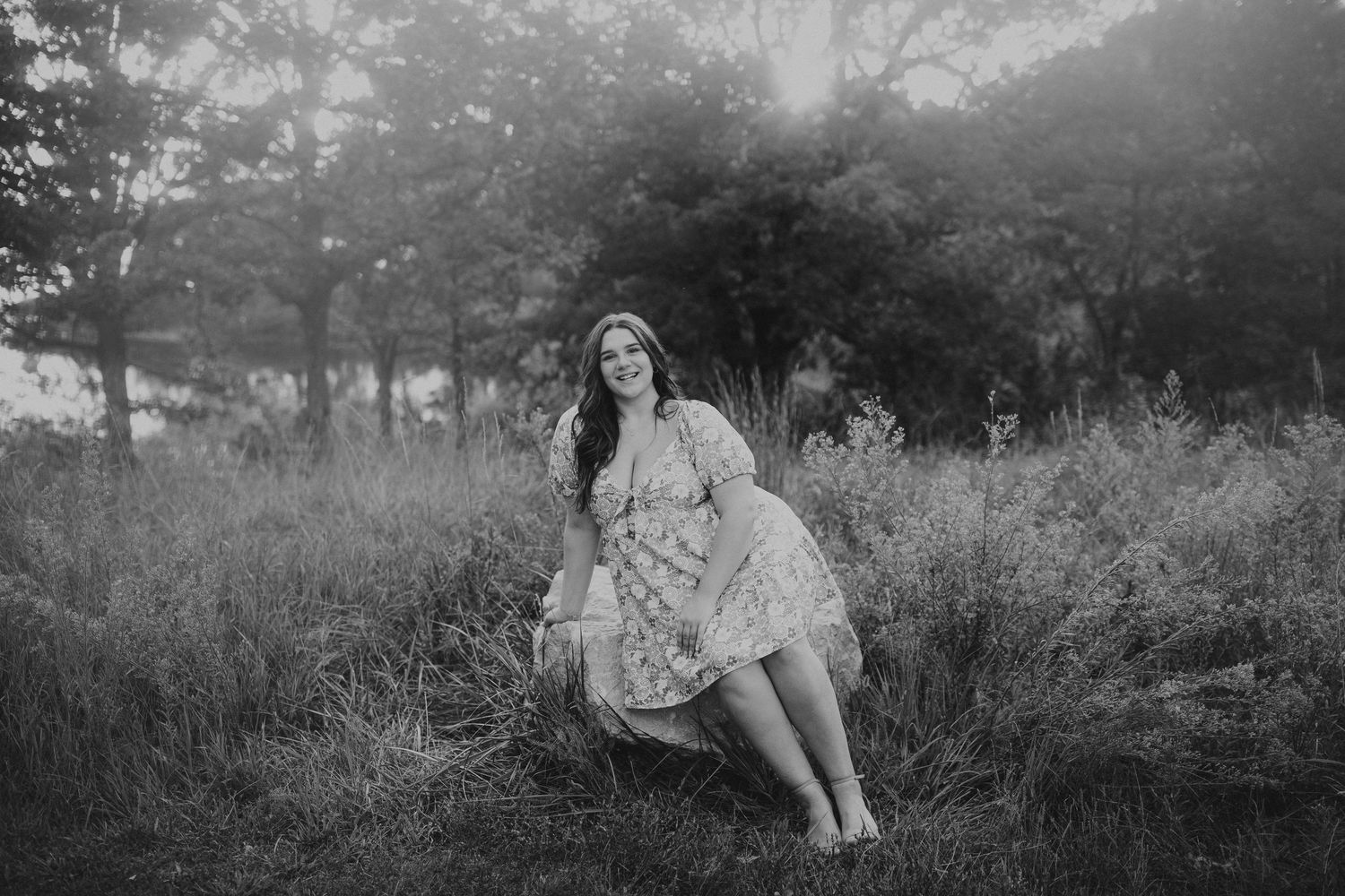 summer senior photos of girl in dress siting on rock in tall grass field