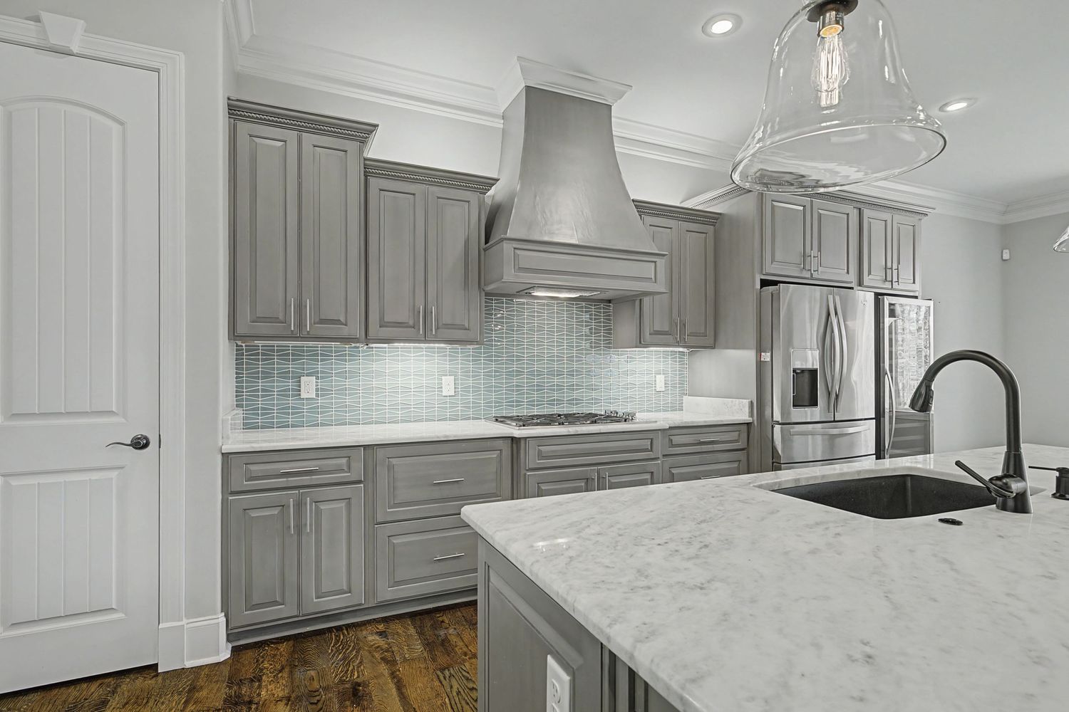 Modern white kitchen remodel features marble countertops, gray cabinets, and pendant lighting in an open concept space.