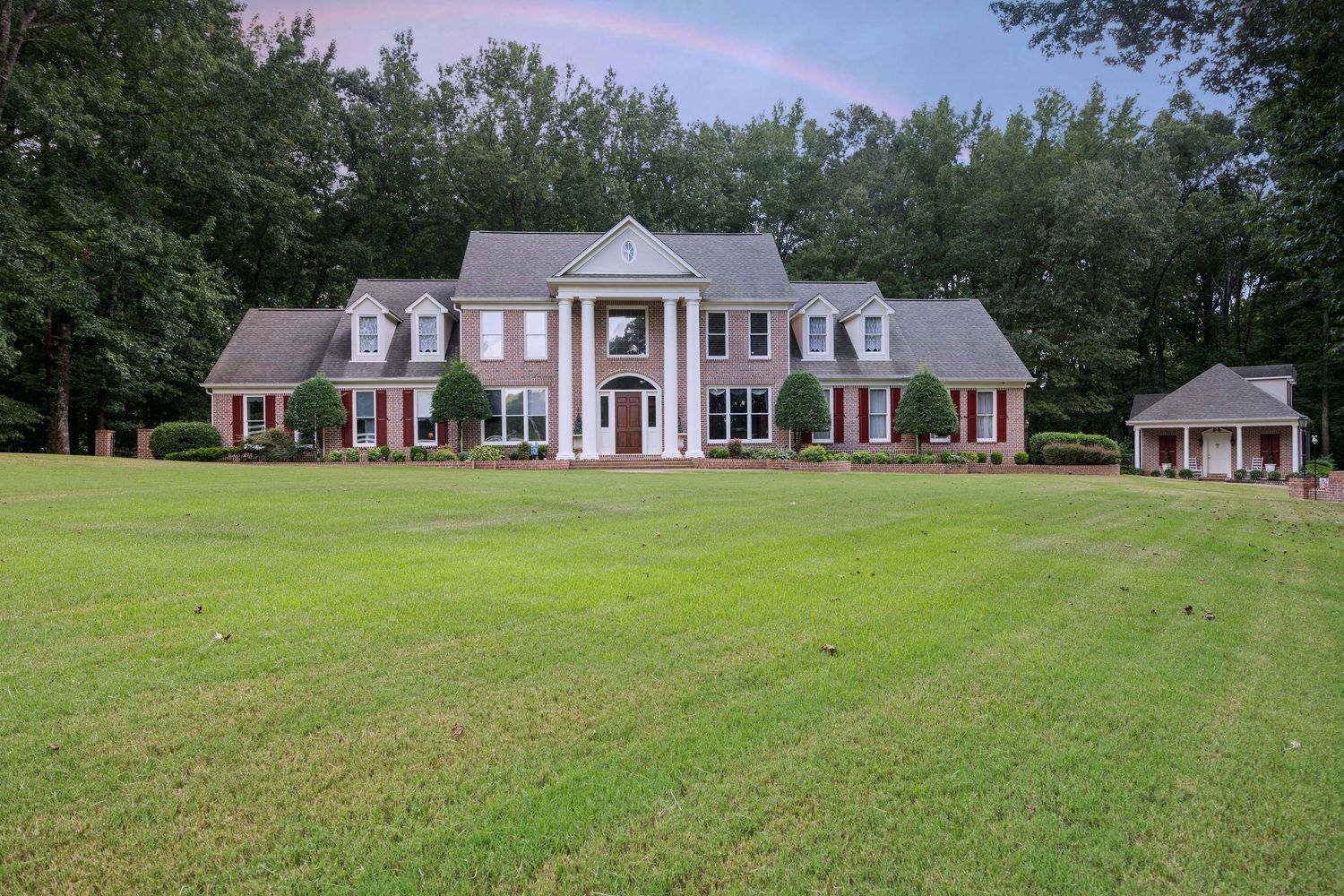 Panoramic view of a stately brick colonial home with white columns and manicured lawn.