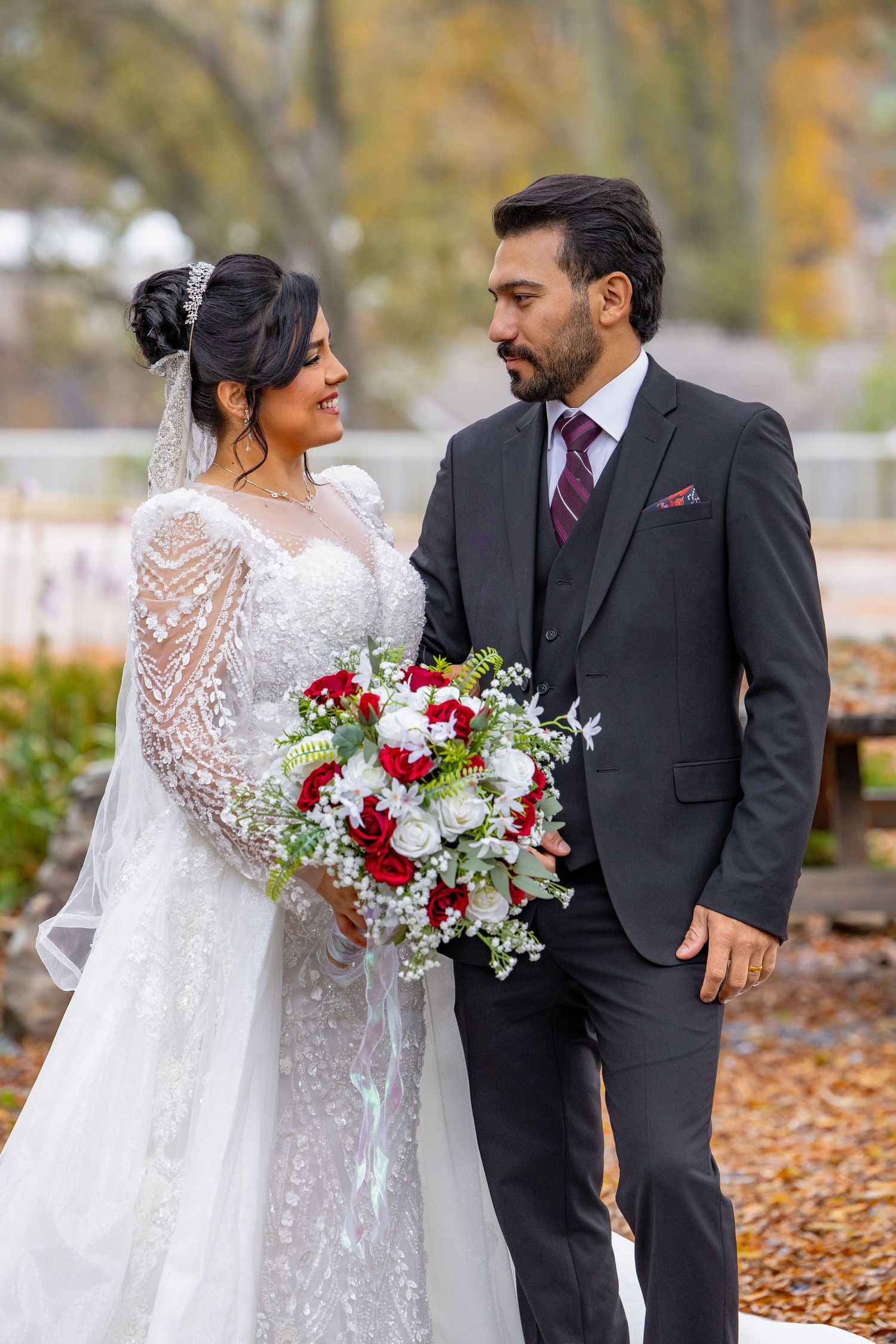 Autumn wedding portraits with red and white bouquet against colorful fall leaves background.