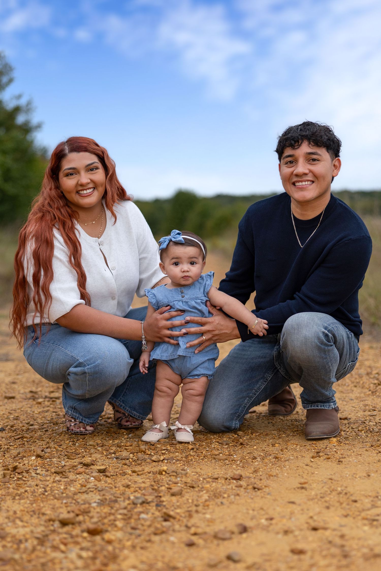 Family sitting together on a dirt path surrounded by natural landscape on a bright day.