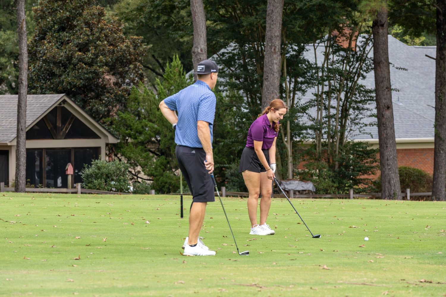 Players putting on a golf course surrounded by pine trees.