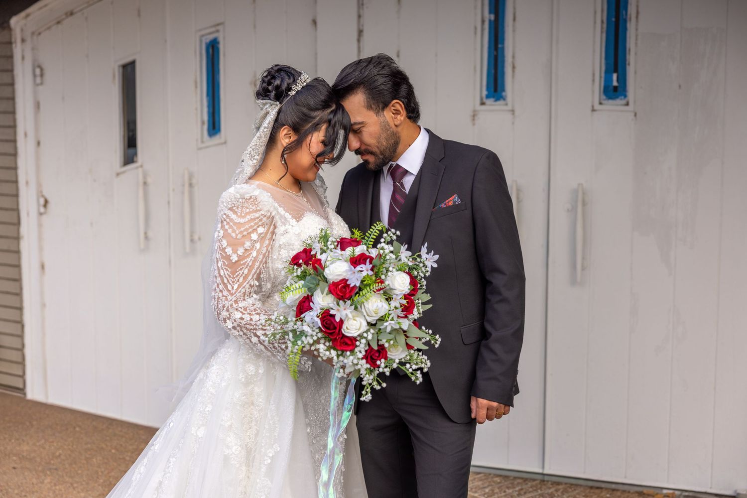 Elegant wedding couple sharing a romantic moment against a white wall backdrop.