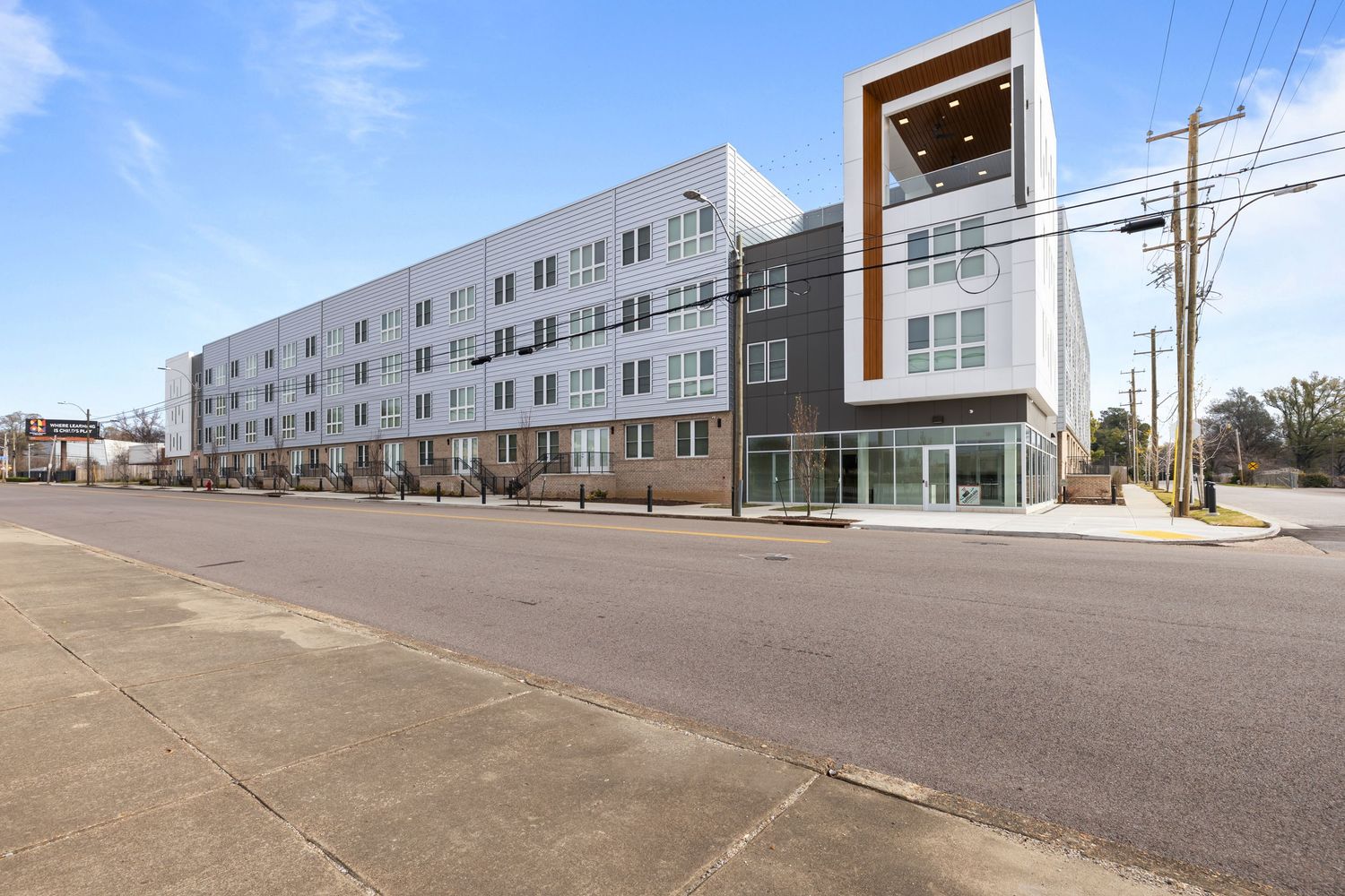 Modern apartment building with white and gray exterior features a distinctive corner entrance and large windows on a city street.