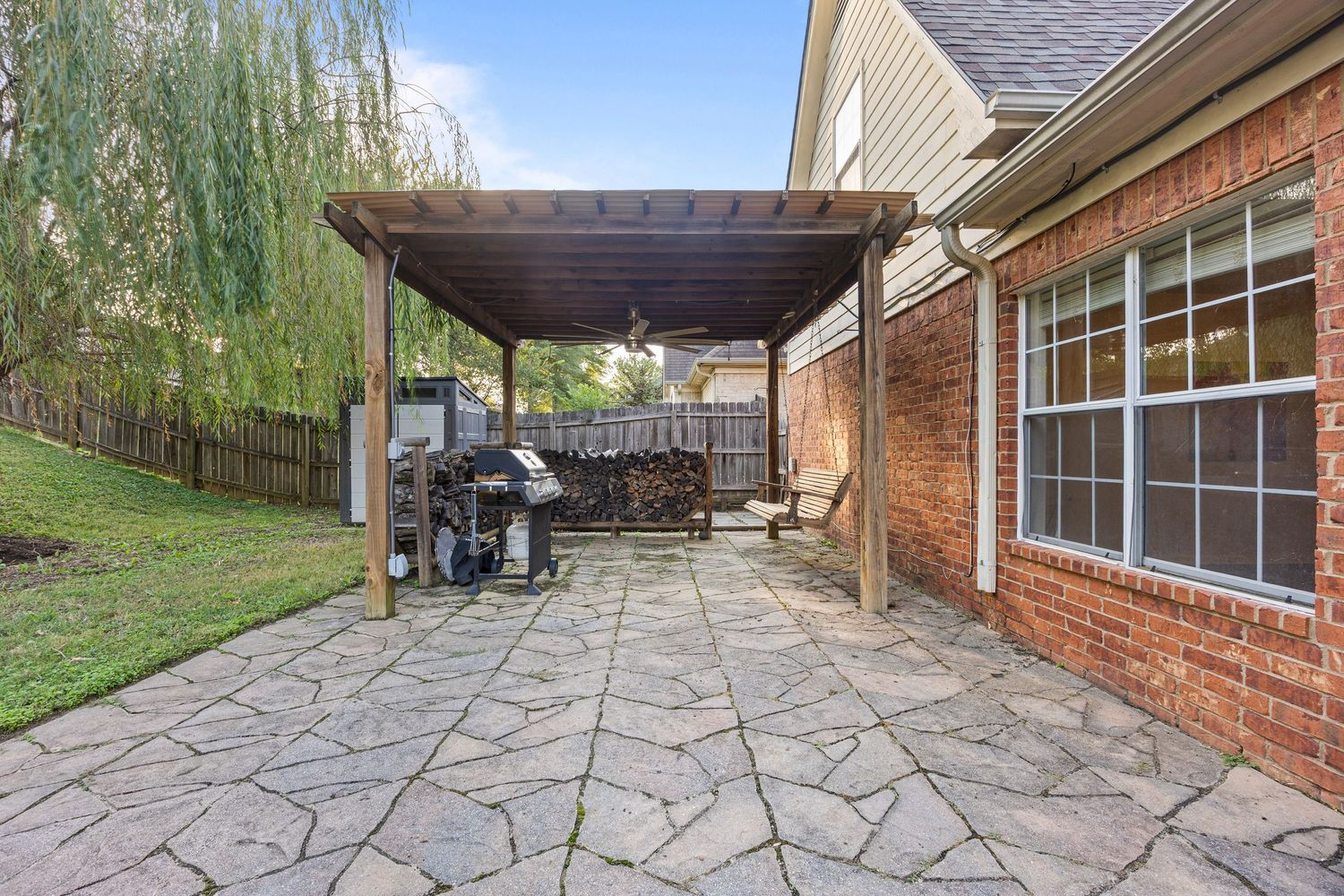 A series of connected outdoor stone patios and walkways with brick walls and overhanging trees create a peaceful garden setting.