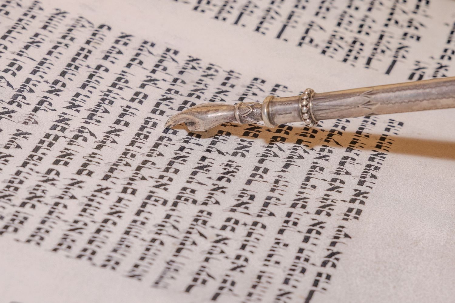 A silver yad Torah pointer resting on an open Hebrew Torah scroll with ancient Jewish text.