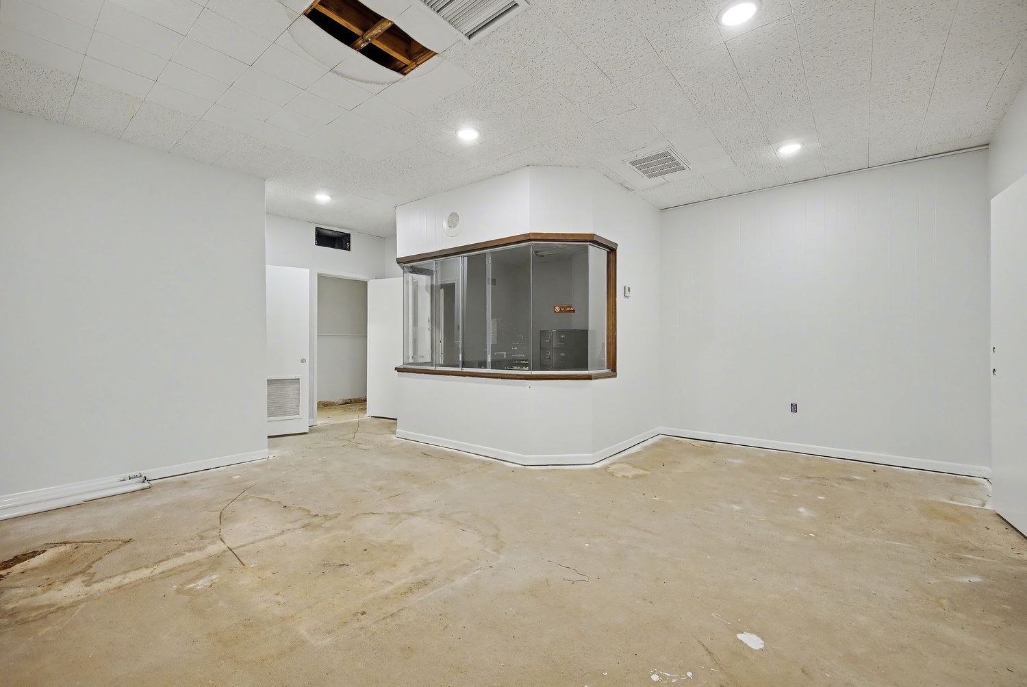Empty white basement room with recessed lighting and unfinished concrete floor under renovation.