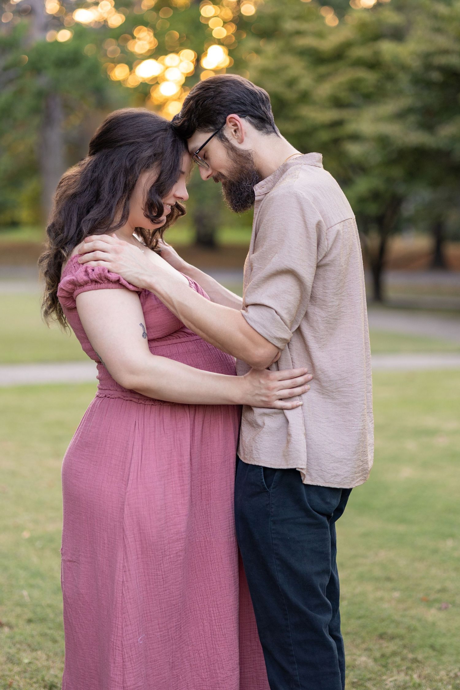 Romantic couple embraces in a park during golden hour with beautiful bokeh lighting in the background.
