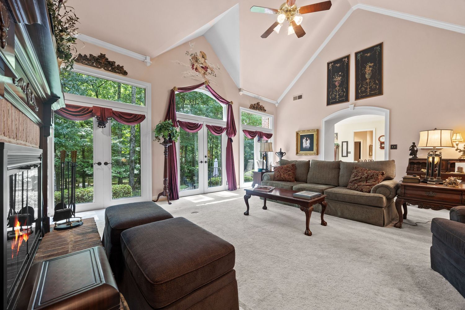 A modern living room with vaulted ceilings features multiple seating areas and large windows overlooking lush greenery.