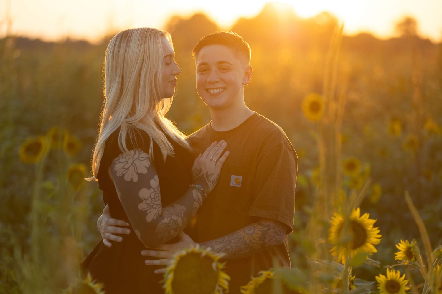 Romantic couple embracing in a sunlit sunflower field during golden hour sunset.