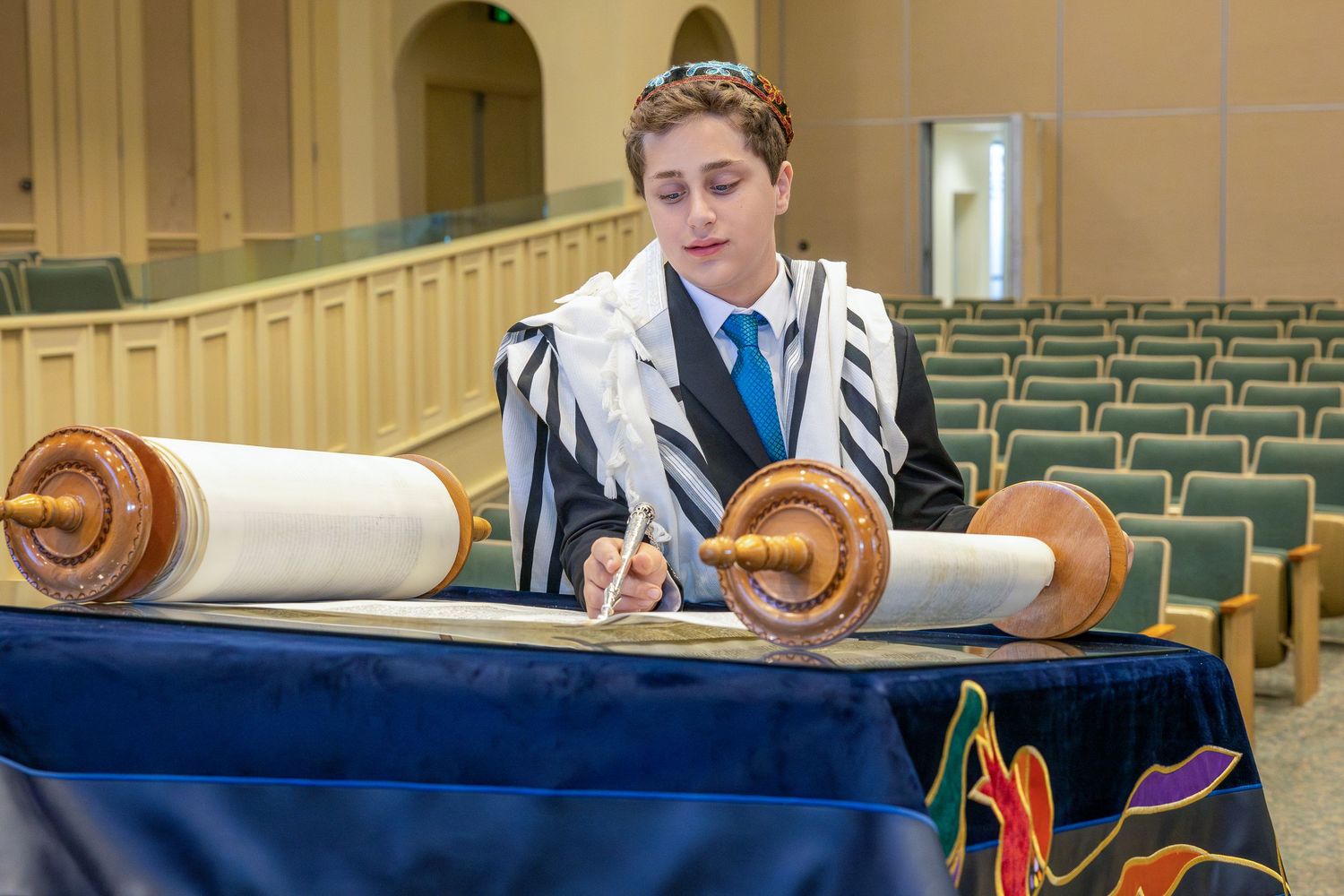 A person in traditional Jewish prayer shawl reads from the Torah scroll during a religious ceremony in a synagogue.