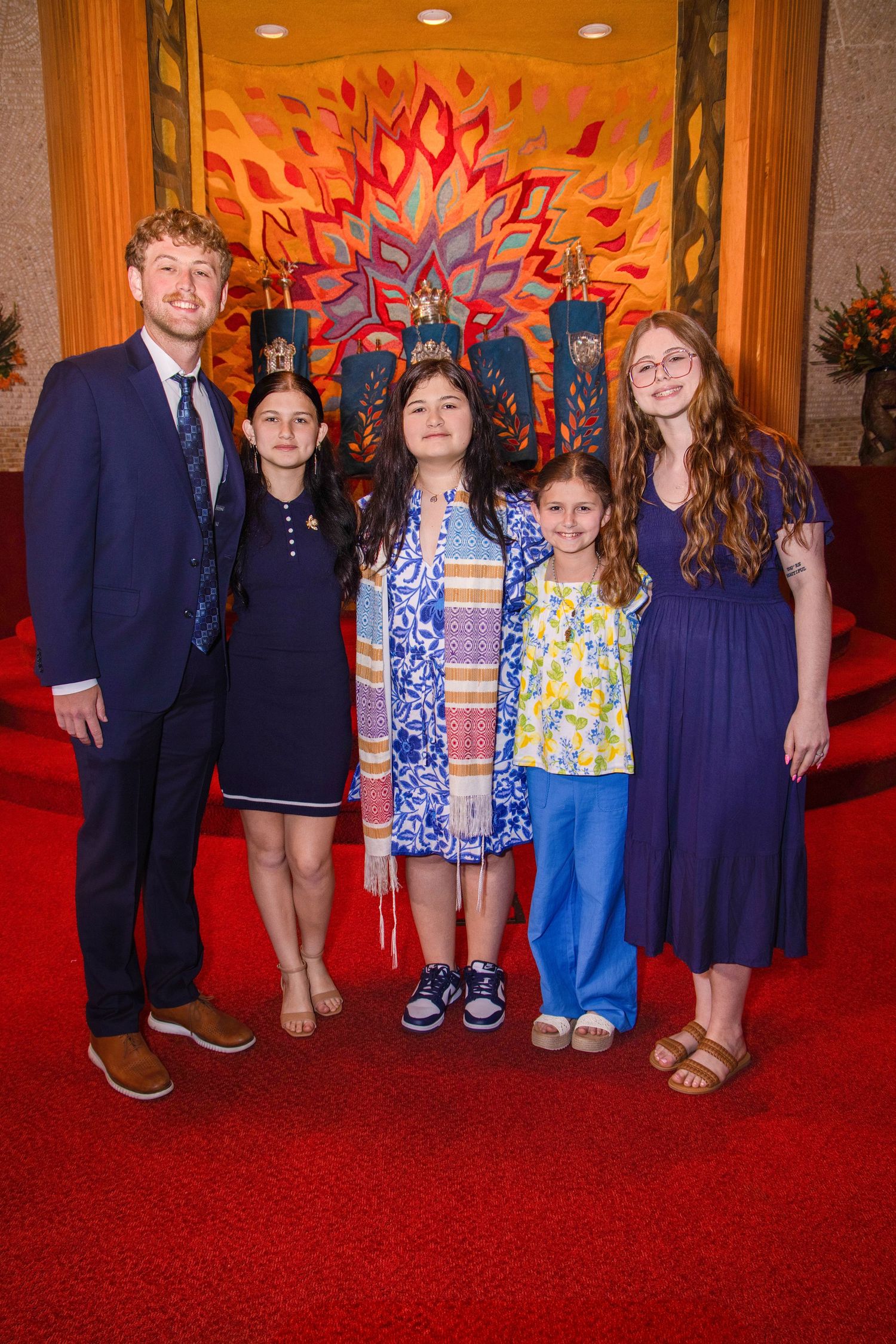 A group stands in front of a vibrant red and orange starburst wall art display on a red carpeted floor.