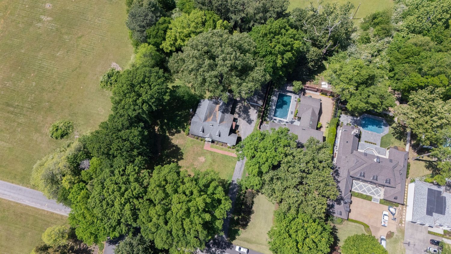 Aerial view of a lush green estate with a large home surrounded by mature trees, pool, and open lawn areas.