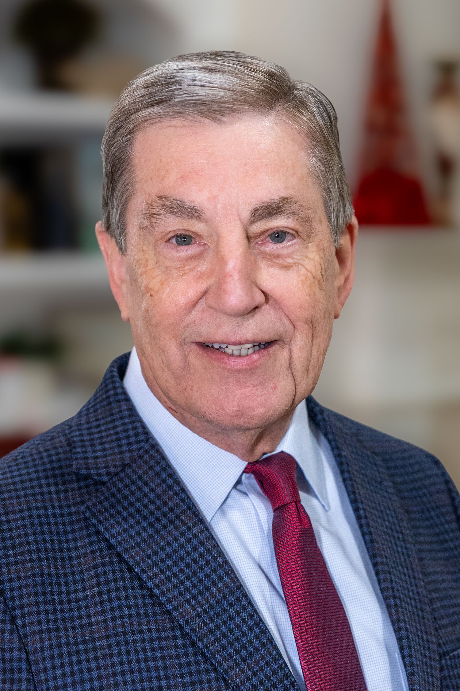 Professional headshot of a senior gentleman in a plaid blazer and red tie.