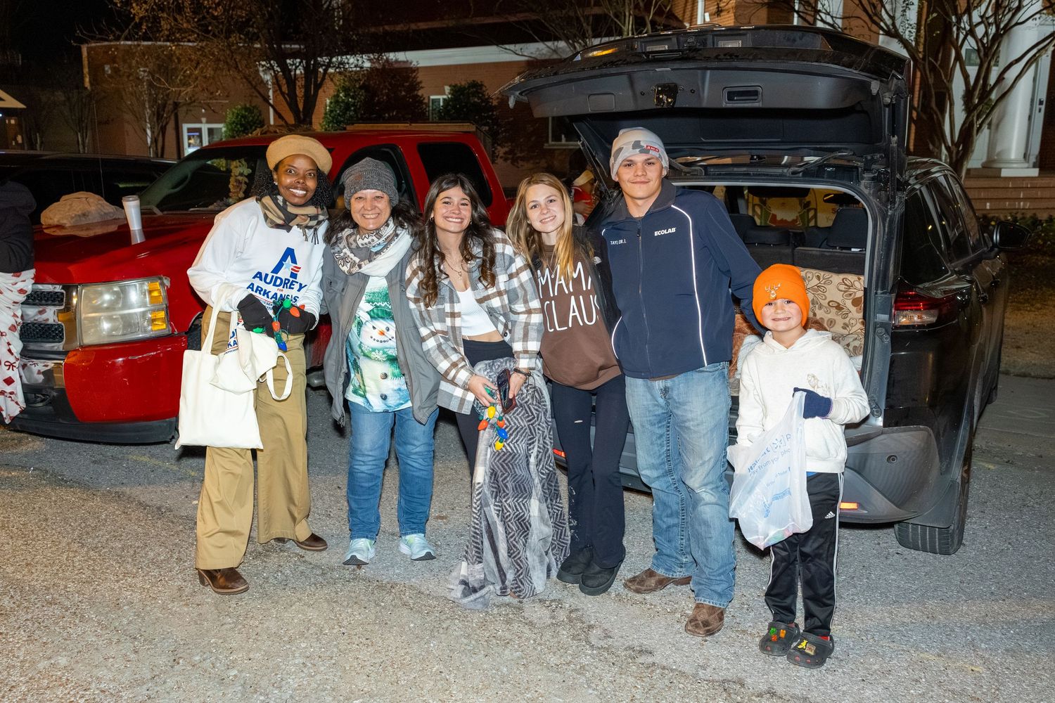Group photo of attendees with a vehicle at a nighttime community event.